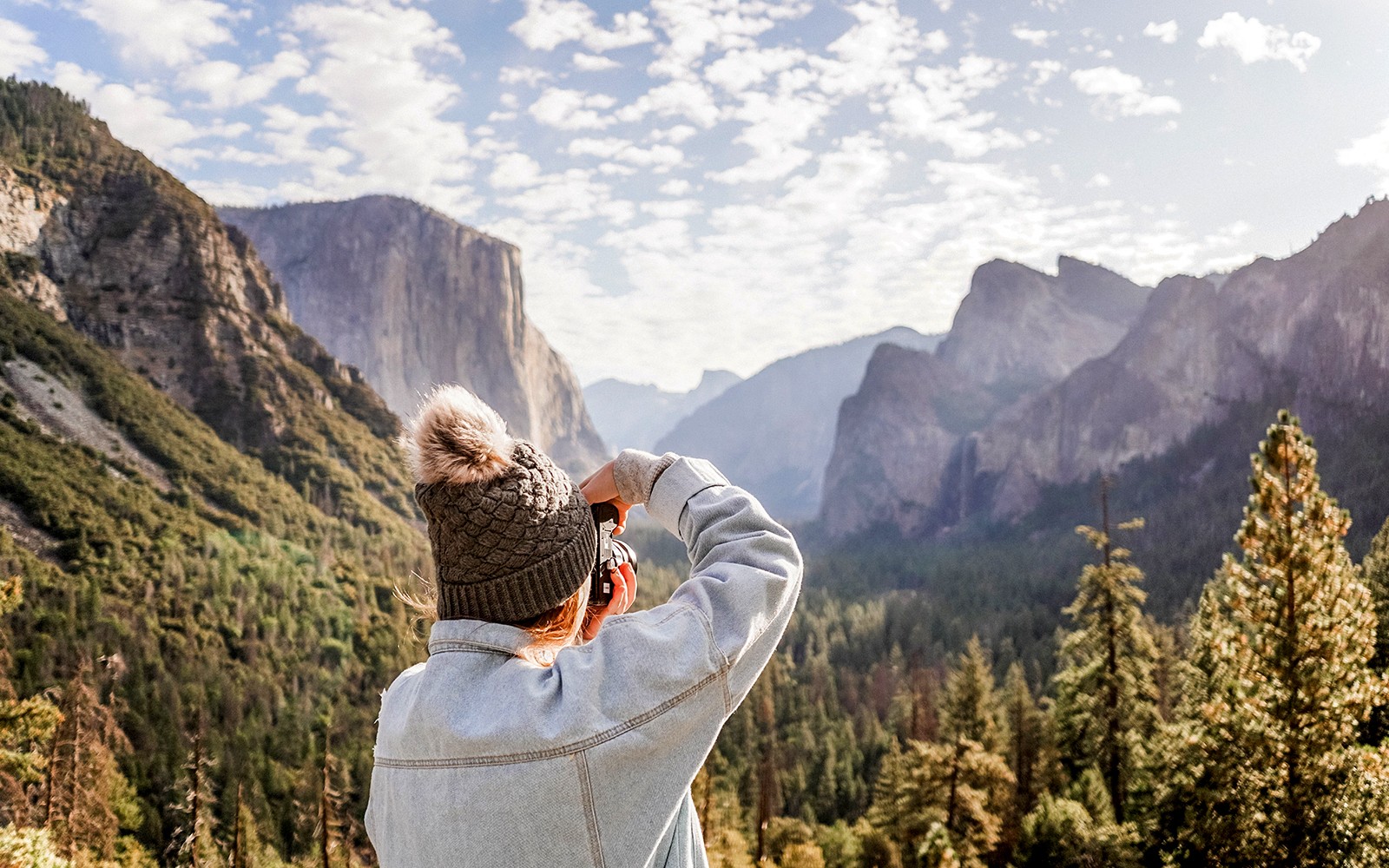Person photographing Yosemite Valley's cliffs and forest.