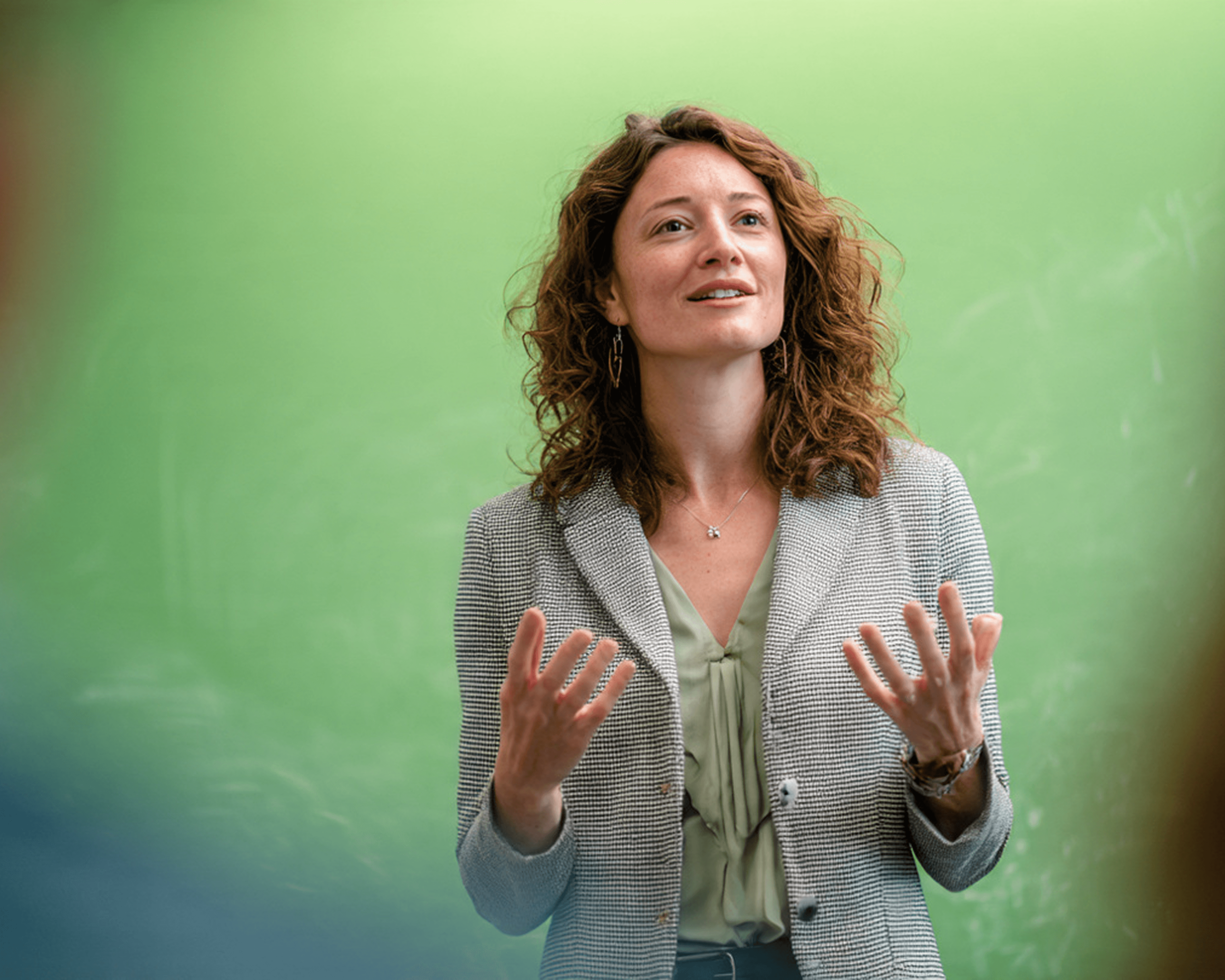 Person in checkered blazer speaking in front of chalkboard