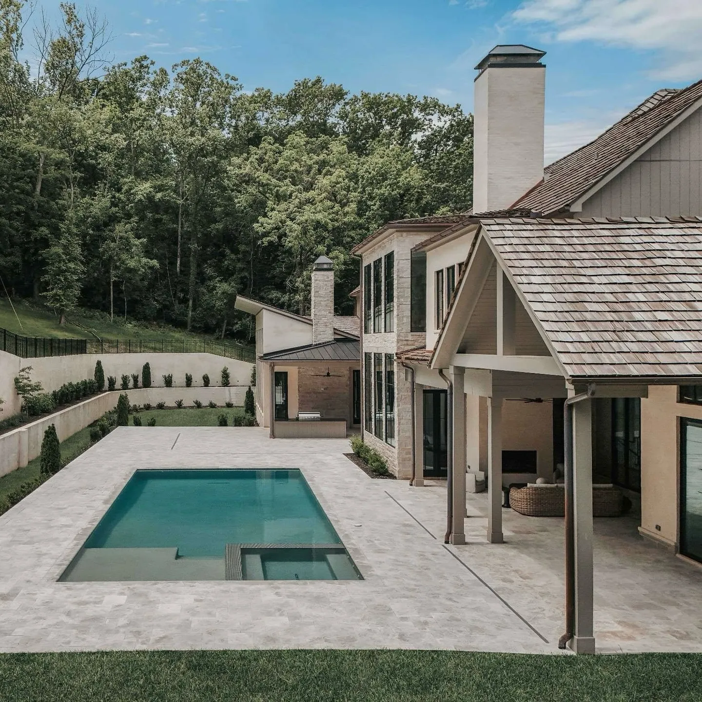 An outdoor pool area with a luxurious house and surrounding greenery.