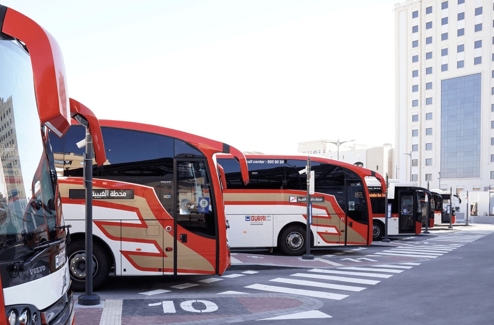 Dubai public buses in Jumeirah parked at a station, showing red and beige transit coaches lined up along marked lanes.