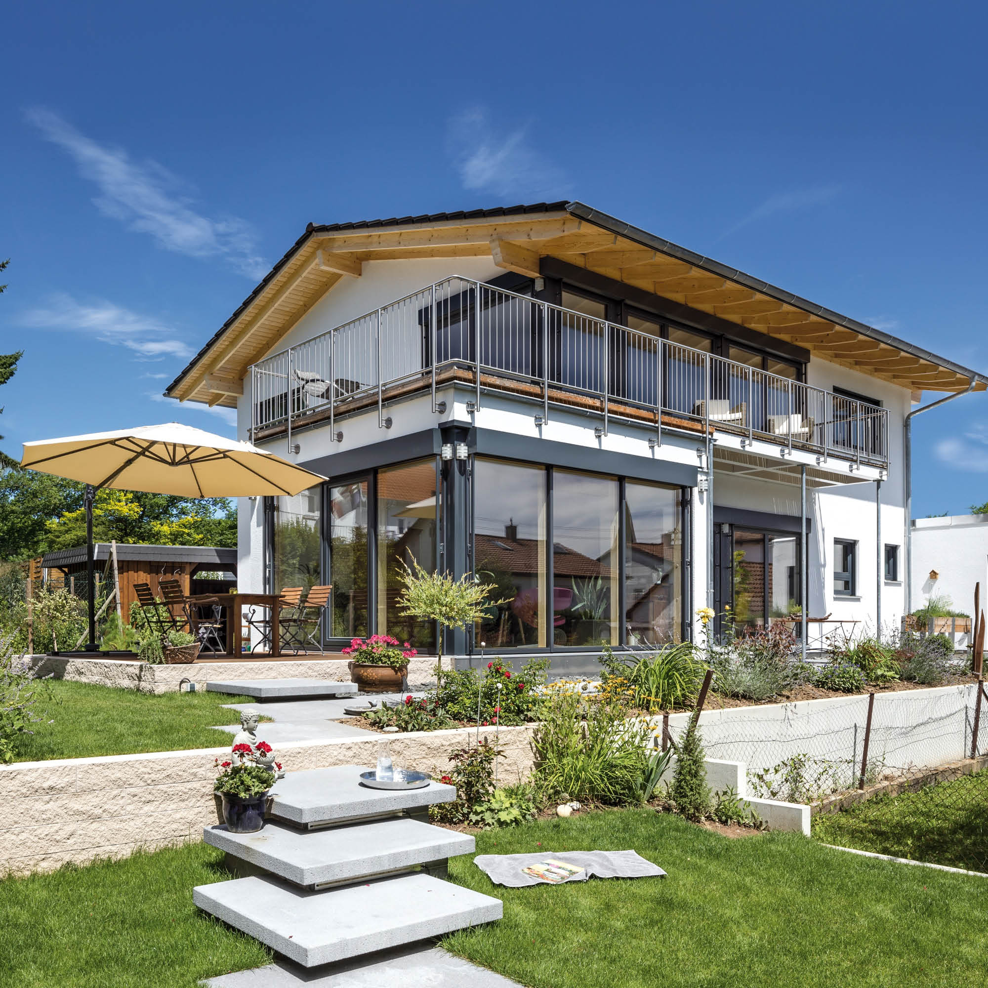 Modernes Einfamilienhaus mit großzügiger Balkon und Terrasse, umgeben von gepflegtem Garten mit Blumen und Rasenflächen.