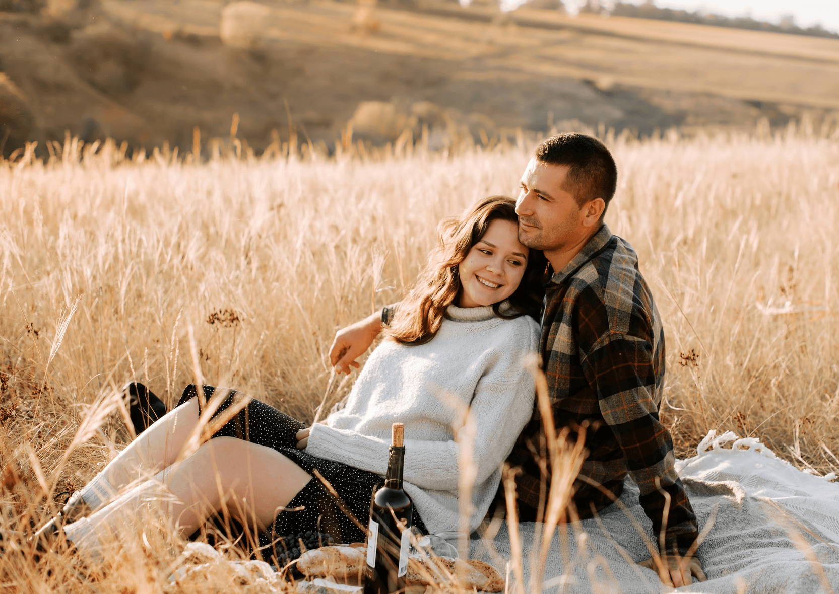 Verliebtes Paar auf einer Spätsommerwiese, umringt von hellen Strohhalmen, blicken in den Sonnenuntergang
