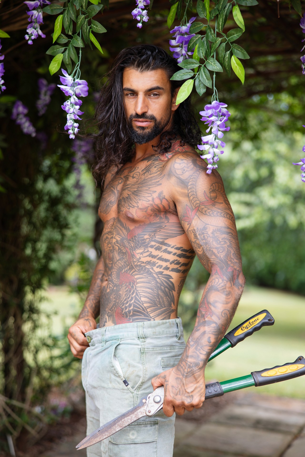 Shirtless man under jacaranda vine holding hedge shears