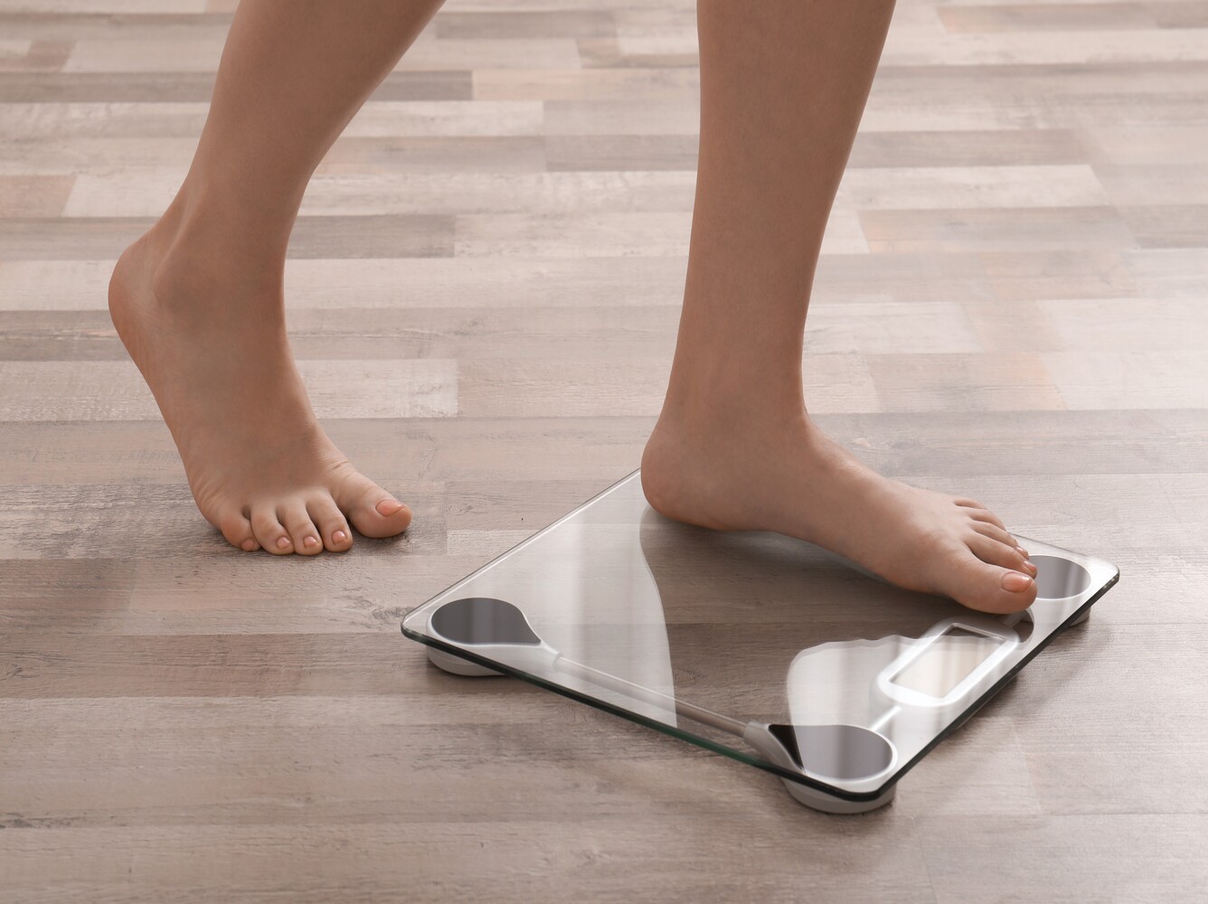 woman stepping on a scale at home to check her progress from using the best vibration plate for weight loss