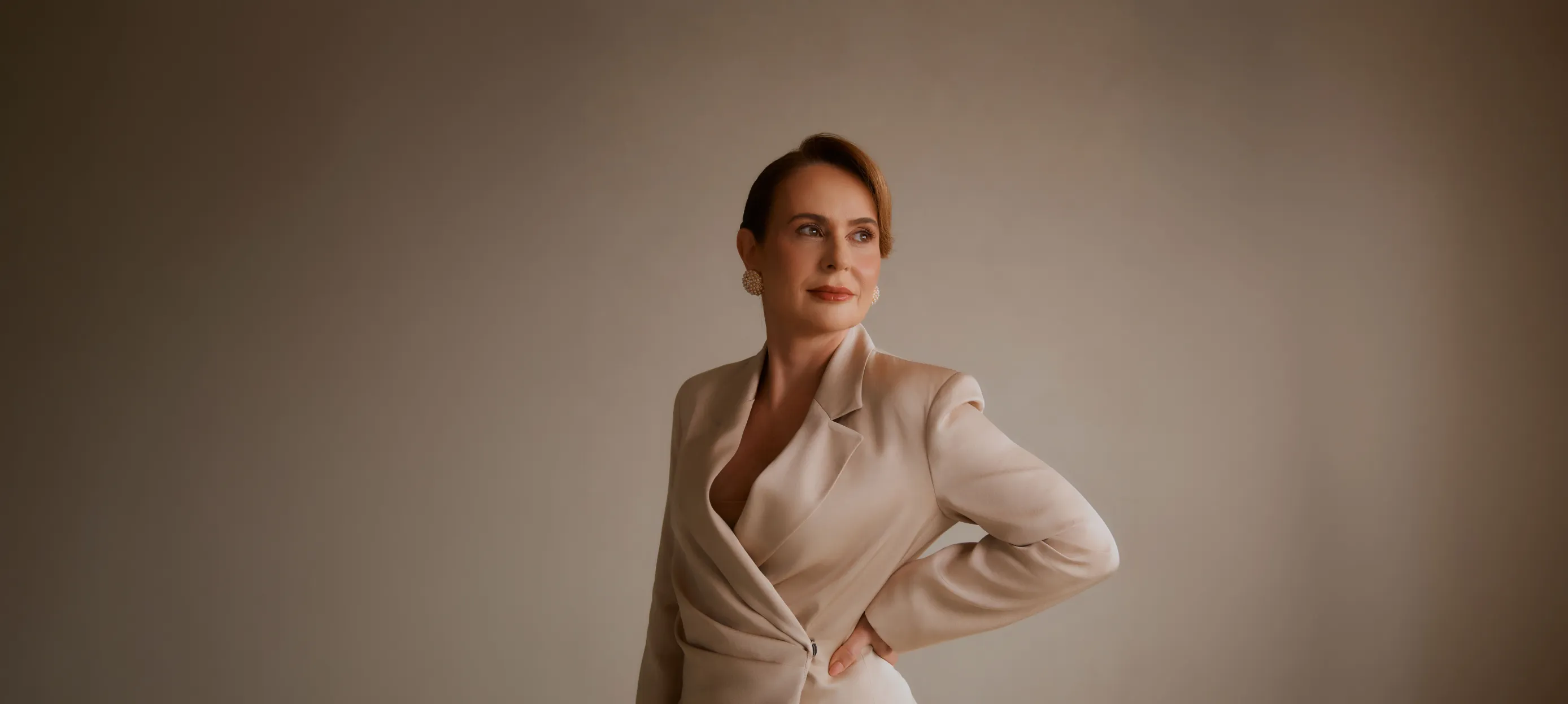 Woman in profile wearing a white turtleneck and red hoop earring against a blue background