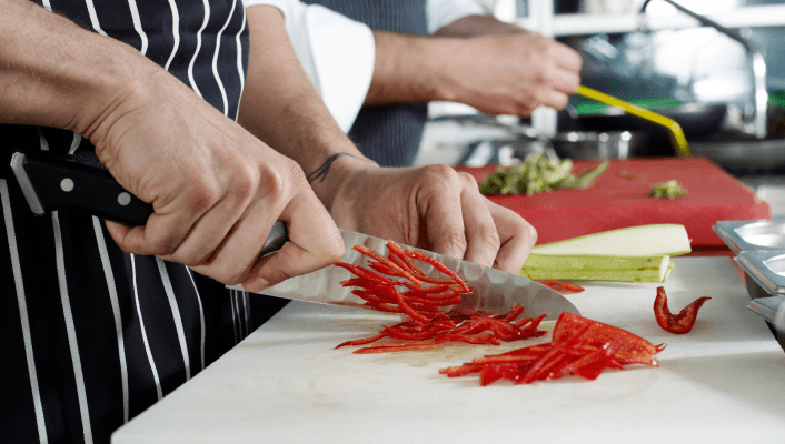 Chef slicing red peppers on cutting board in kitchen.