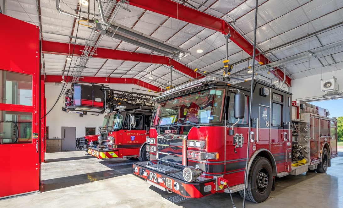 Apparatus bay interior with fire engine and exposed red steel structure at Hewitt Fire Station 2, by Martinez Architects