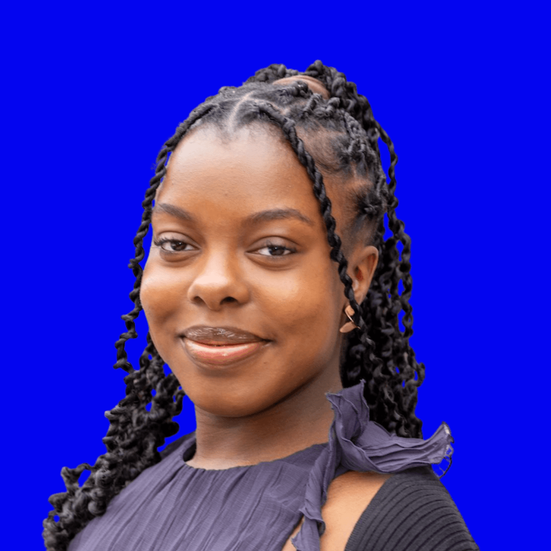 A smiling person with braided hair stands in front of a bright blue background.