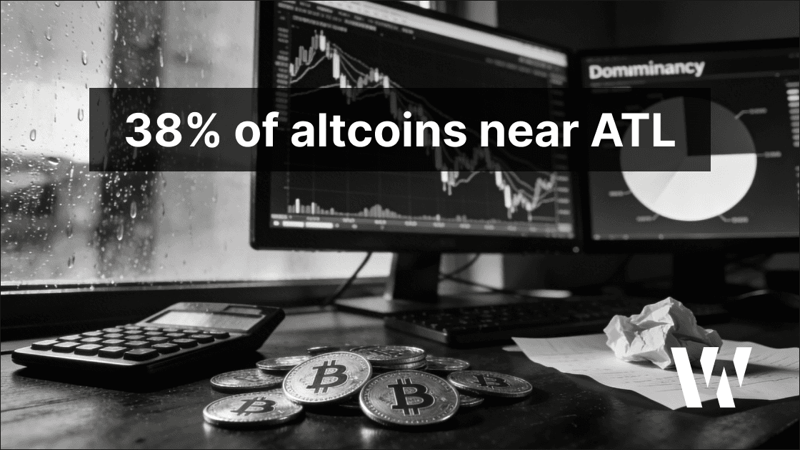 Black-and-white editorial photo of a crypto trading desk showing altcoins near all-time lows, plunging multi-asset charts, and rising Bitcoin dominance, with generic metal crypto coins, a calculator, crumpled notes, and rain-streaked window reflections in moody film-noir lighting.