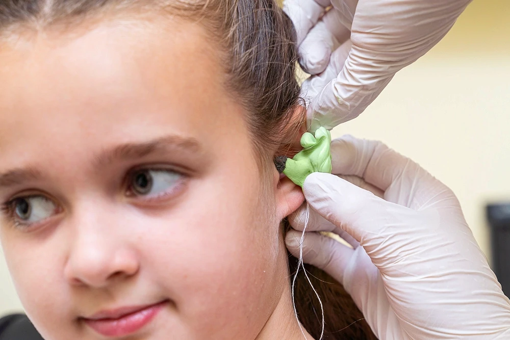 A woman sits at a desk, speaking with another woman through a glass partition in a counseling session.