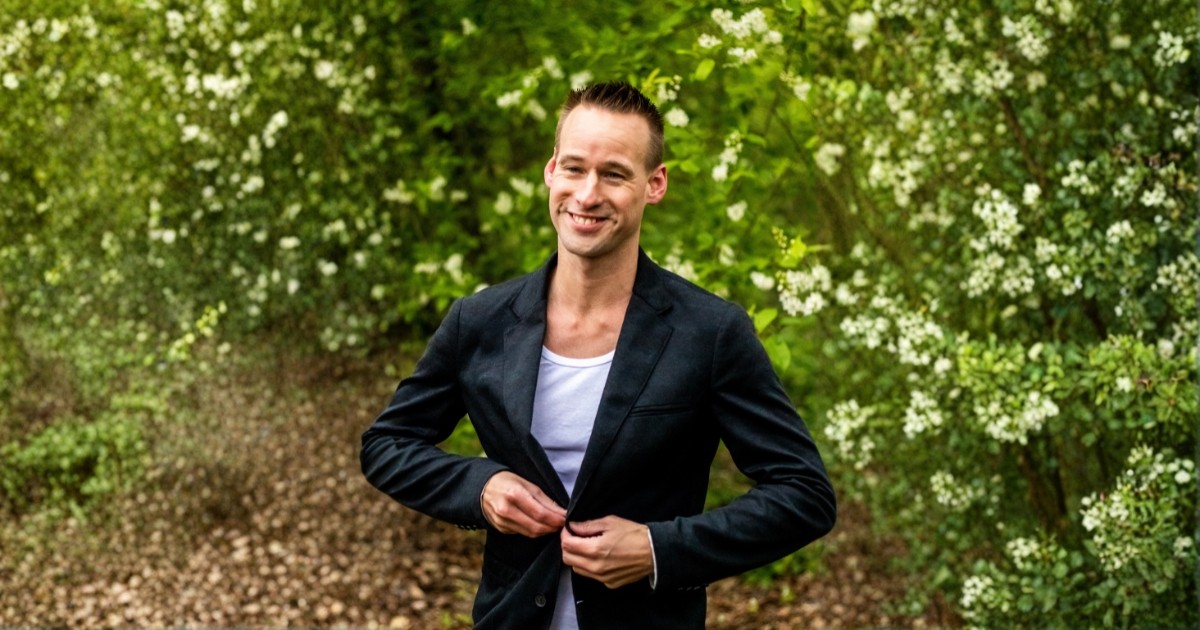 Danny van Brussel, high-end personal trainer voor ondernemers, in zwart colbert met lichte shirt, glimlachend tegen een donkere achtergrond.