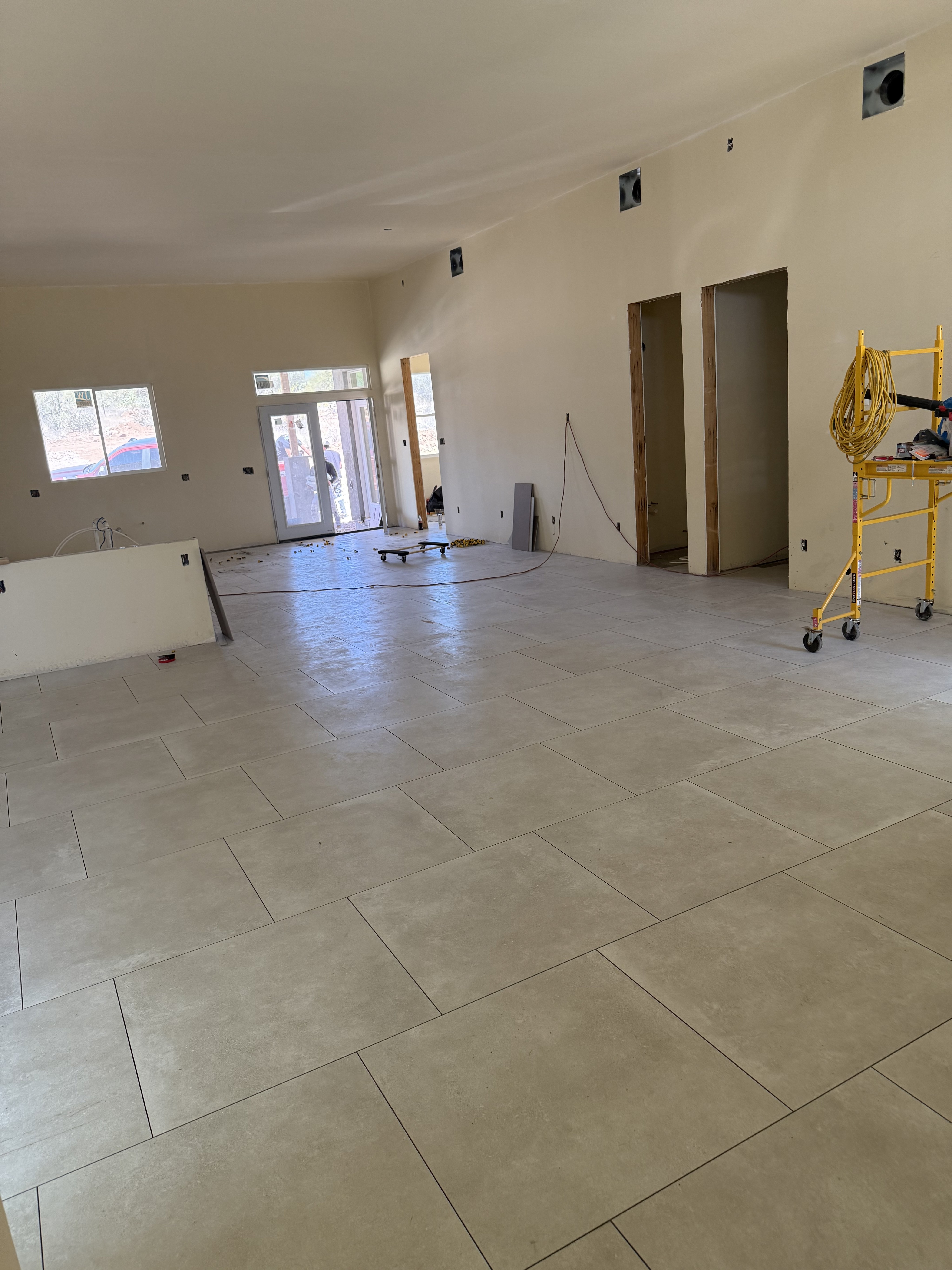 Modern living area with gray wood-look tile flooring, large sliding glass doors, and open space in a new home under construction.