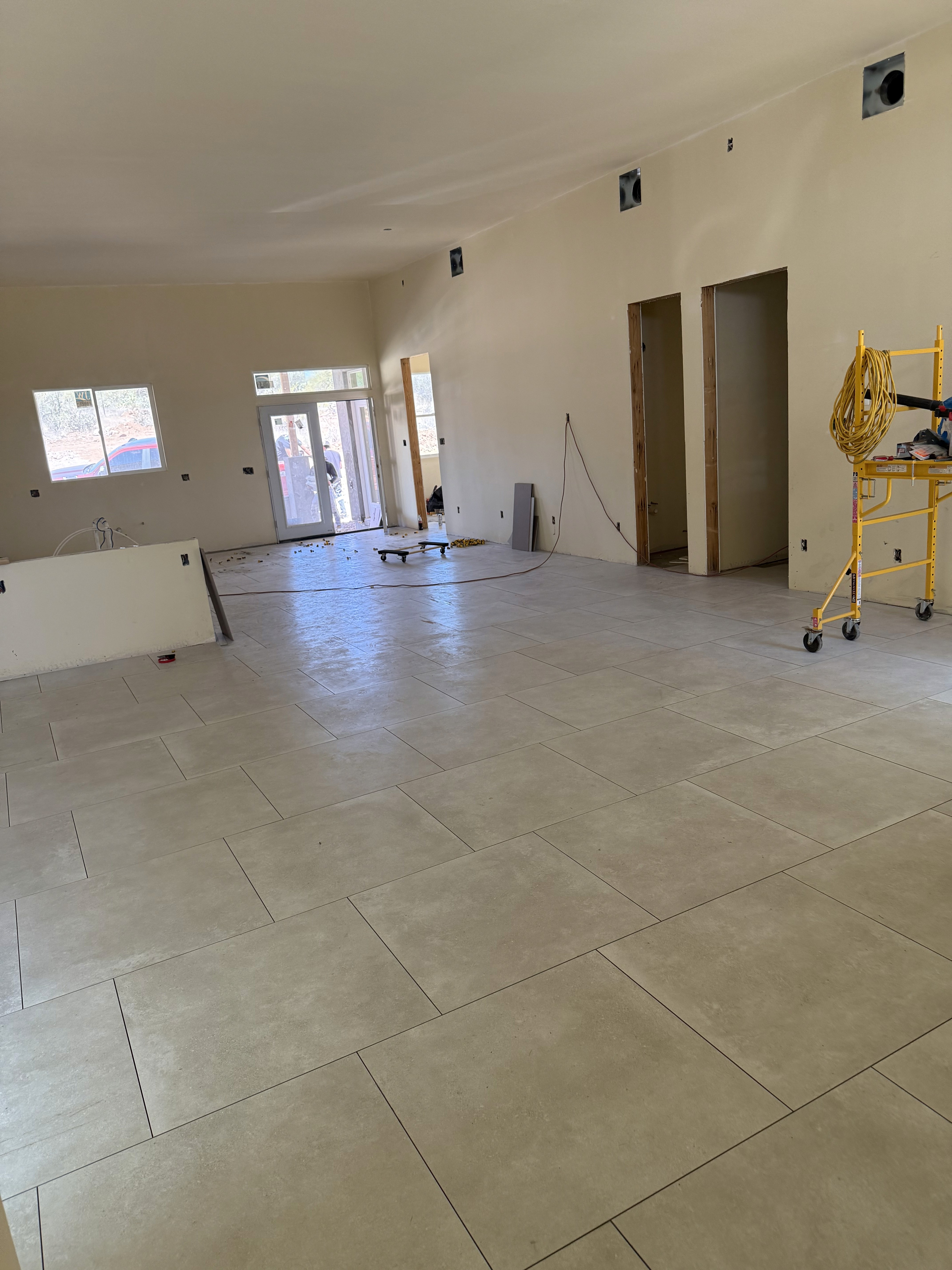 Modern living area with gray wood-look tile flooring, large sliding glass doors, and open space in a new home under construction.