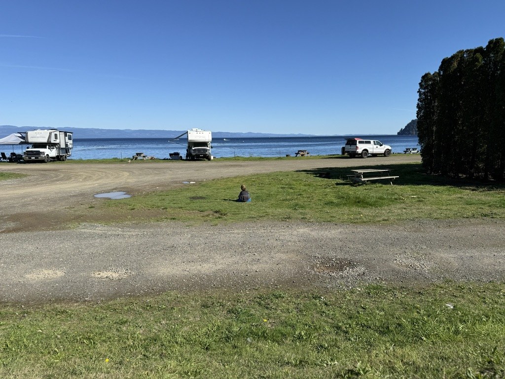 Hyrum sits in the grass at a roomy waterfront campground, with RVs spaced apart.