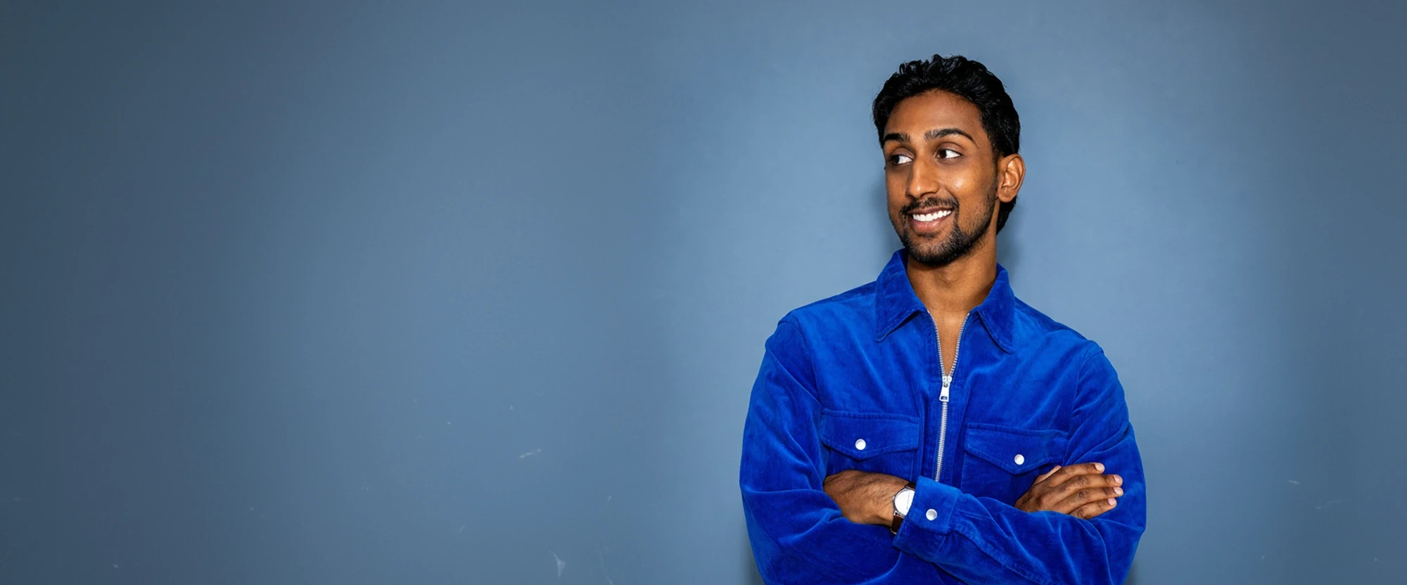 Christian Harinarain, Growth Lead at V7, standing against a blue wall with his arms folded