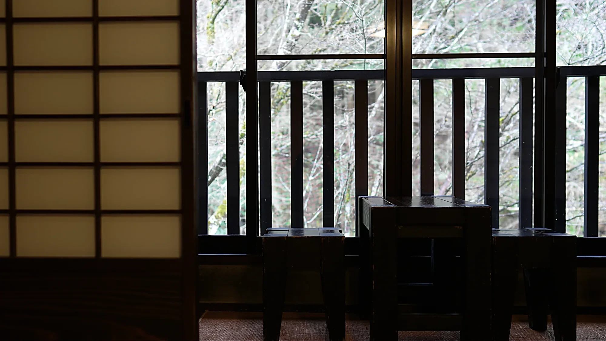 A two-storey timber inn facade at Kurokawa Onsen seen behind maples