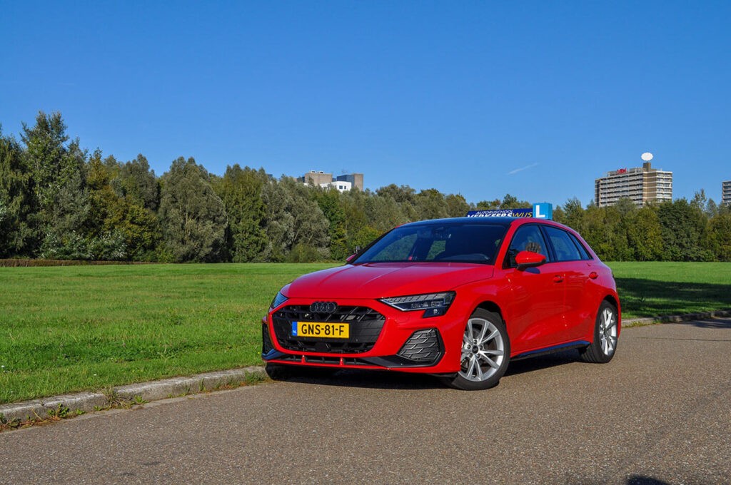 A smiling young man with crossed arms, wearing a plaid shirt and white t-shirt, poses against a dark background.