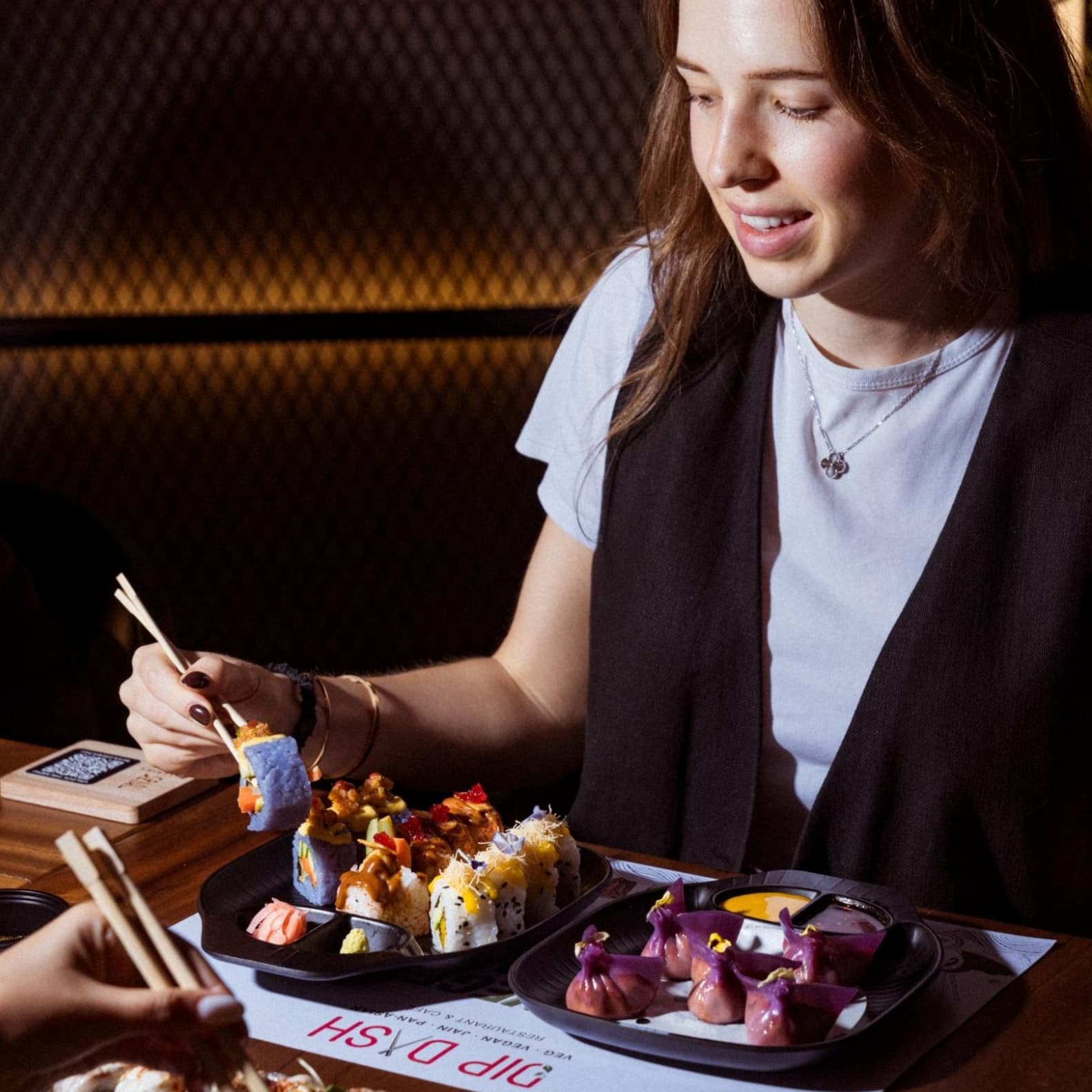 A woman eating vegan foods, sushi and dumplings in Dubai, enjoying colourful plant based dishes in a lively dining space