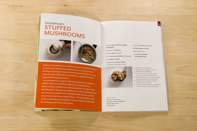 An open cookbook displays a recipe titled "Grandma Jo's Stuffed Mushrooms." The left page features text describing the dish, including its origin from Agata Valentina's kitchen in Brooklyn and Joe Brancaccio's grandmother's recipe. The right page includes a recipe with ingredients and instructions, including chopped parsley, salt, pepper, garlic, onion, bread crumbs, and tomato sauce. The book rests on a light wooden surface.