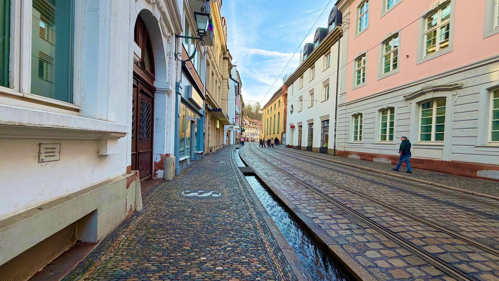 Blick in eine Gasse der Freiburger Altstadt mit Bächle im Kopfsteinpflaster und historischen Häuserfassaden.