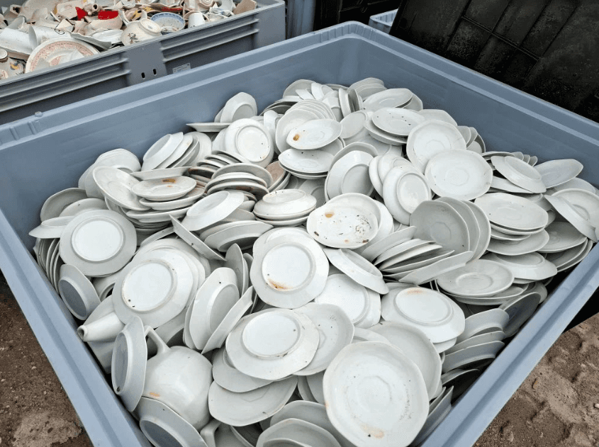 Grand bac industriel gris rempli de centaines d'assiettes et sous-tasses en porcelaine blanche retournées, collectées en vue de leur recyclage