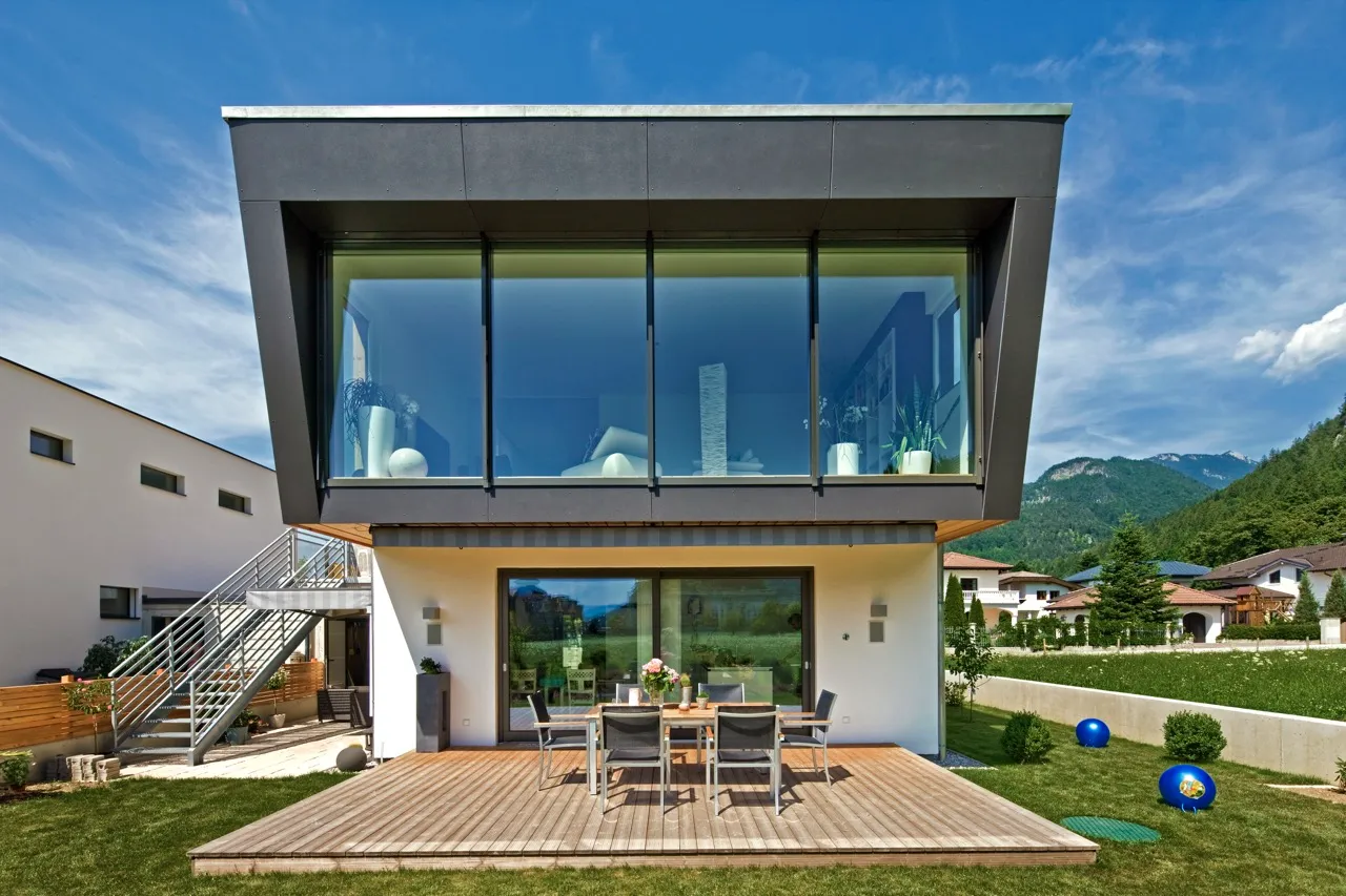 Modernes Einfamilienhaus mit auskragendem Obergeschoss, großen Fensterflächen und Holzterrasse.