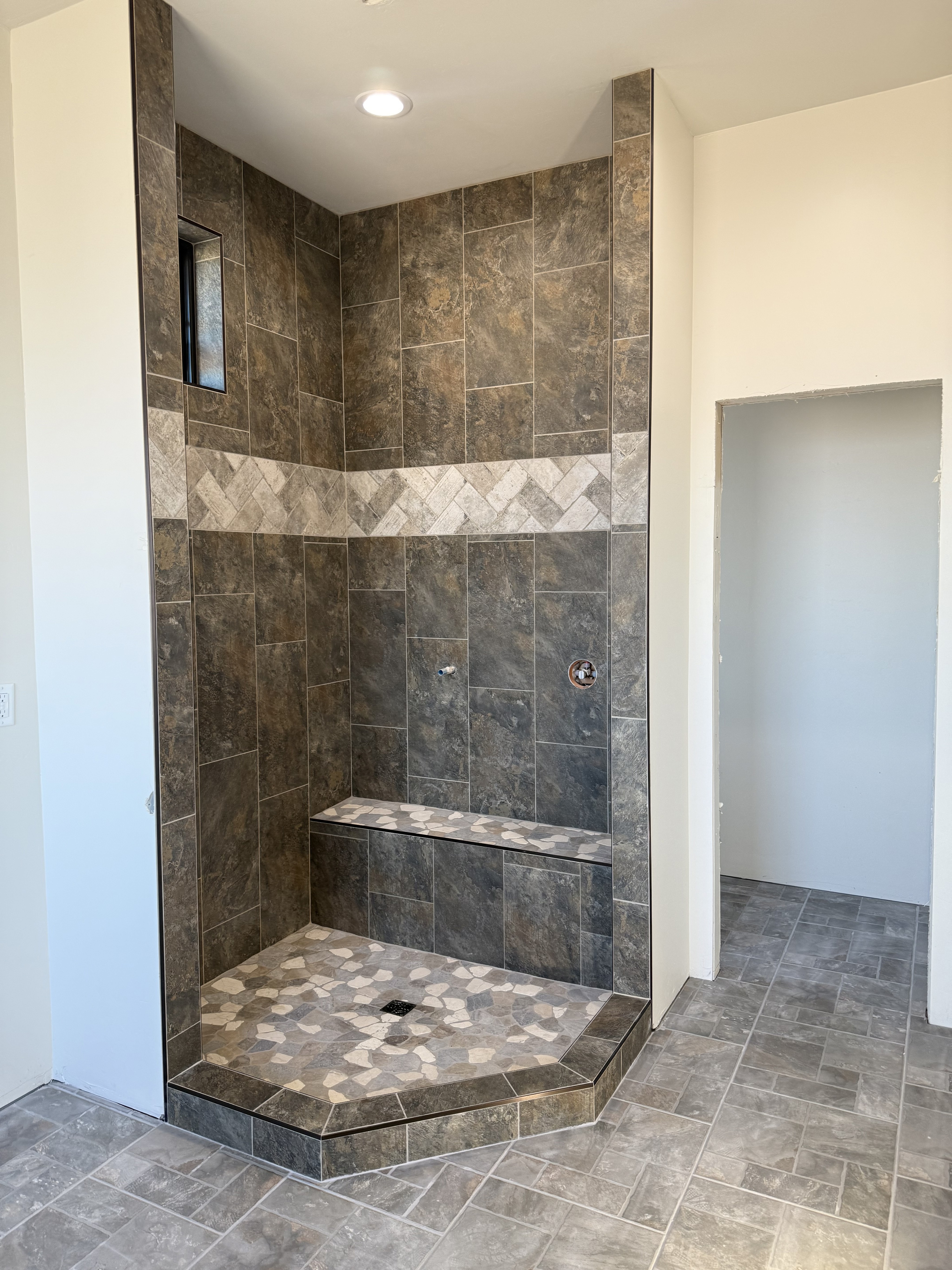 Elegant shower enclosure with white marble-look rectangular wall tiles, a light hexagonal mosaic shower floor, and dark shower fixtures, showcasing a sleek and clean tile design.
