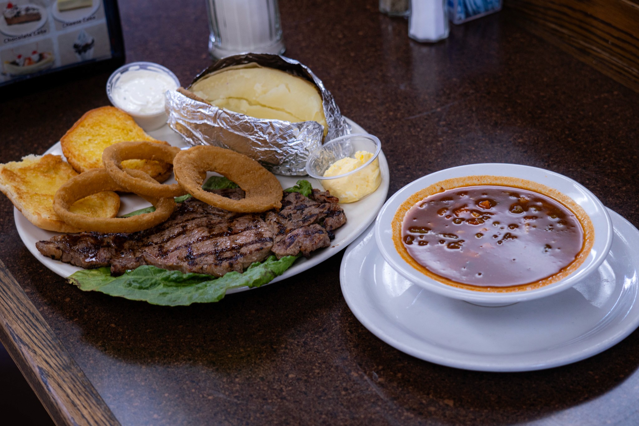 A steak with onion rings, potato, lettuce, sauces, with a mexican stew for lunch at lunch restaurant Harry's Cafe in Stanton, CA on Katella Ave near Disneyland