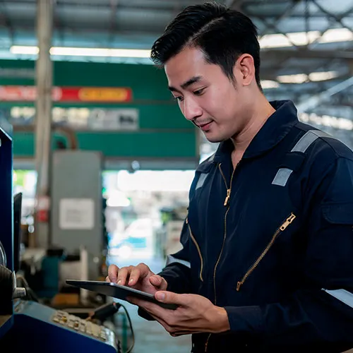 Industrial technician operating machinery while reviewing information on a tablet inside a manufacturing facility.