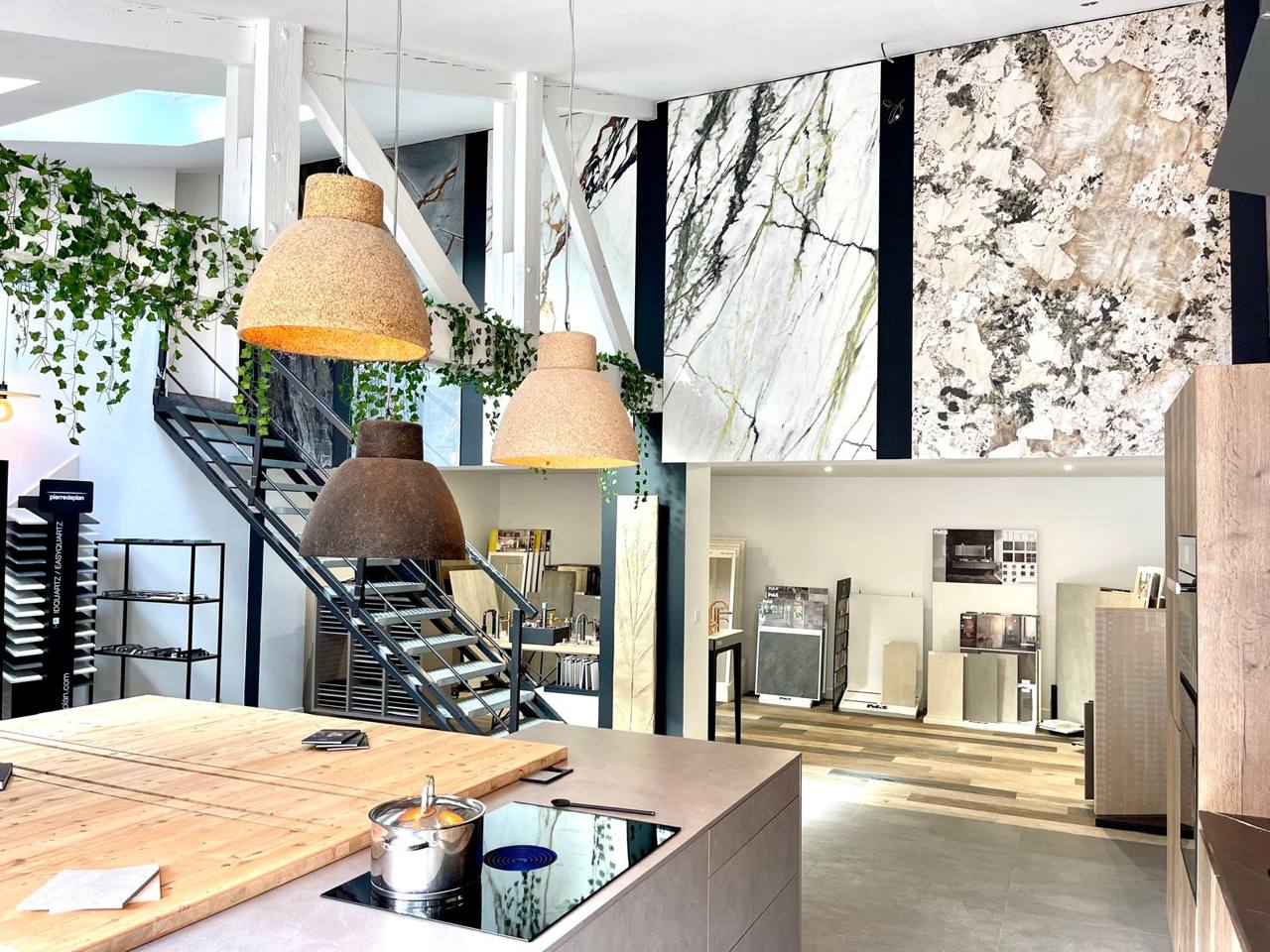 Showroom matériaux Seine-et-Marne avec grandes plaques marbre et pierre, luminaires osier et végétation, conseil architecte d'intérieur.