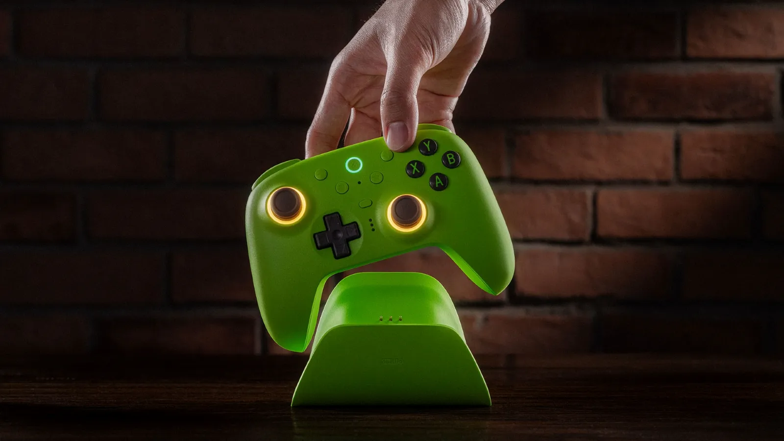 A person places a vibrant green game controller with illuminated joystick rings onto a matching charging station, set against a rustic brick wall background.