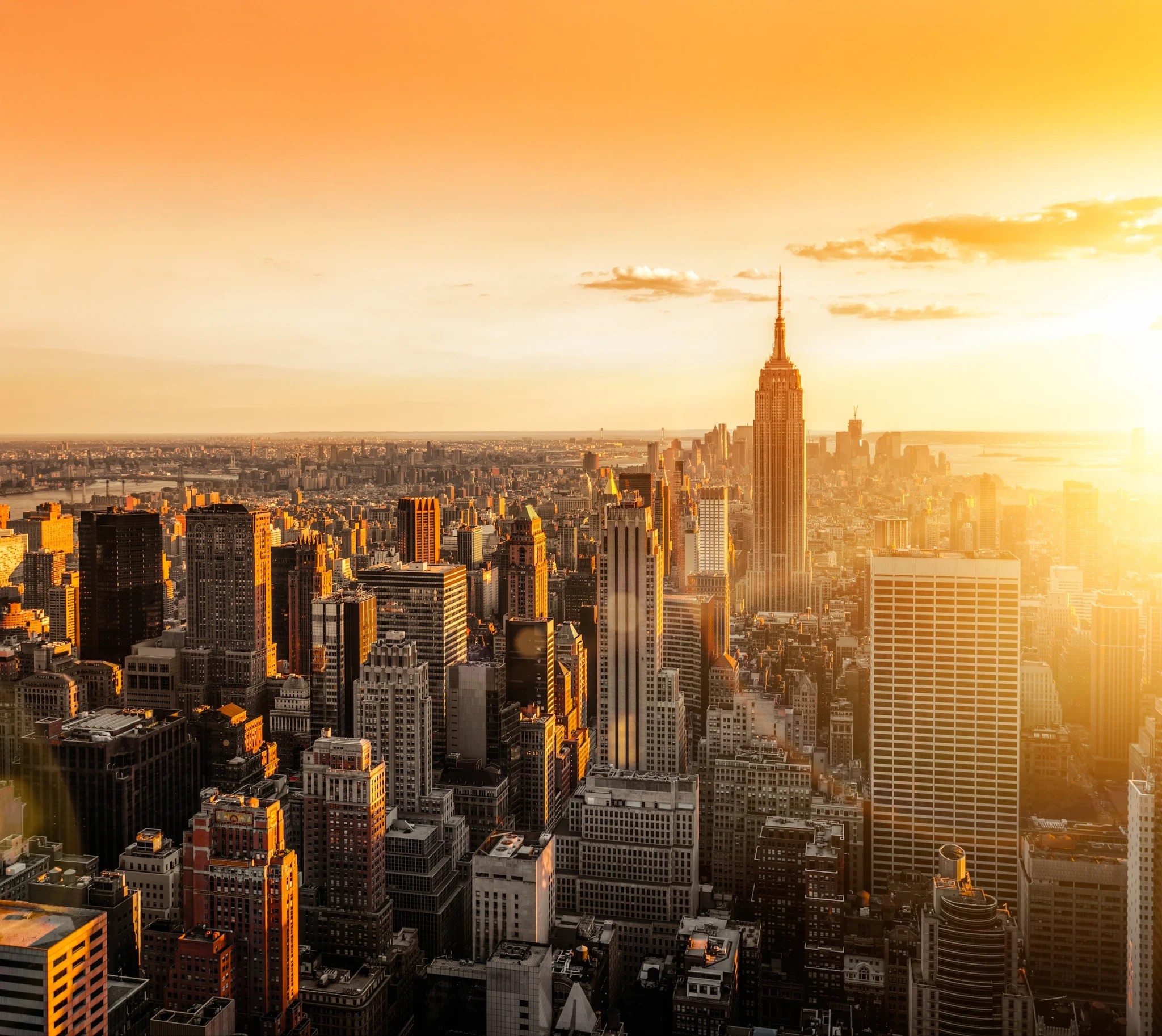 Aerial view of the NYC skyline at sunrise, capturing iconic skyscrapers and the glowing cityscape as the sun rises over Manhattan.
