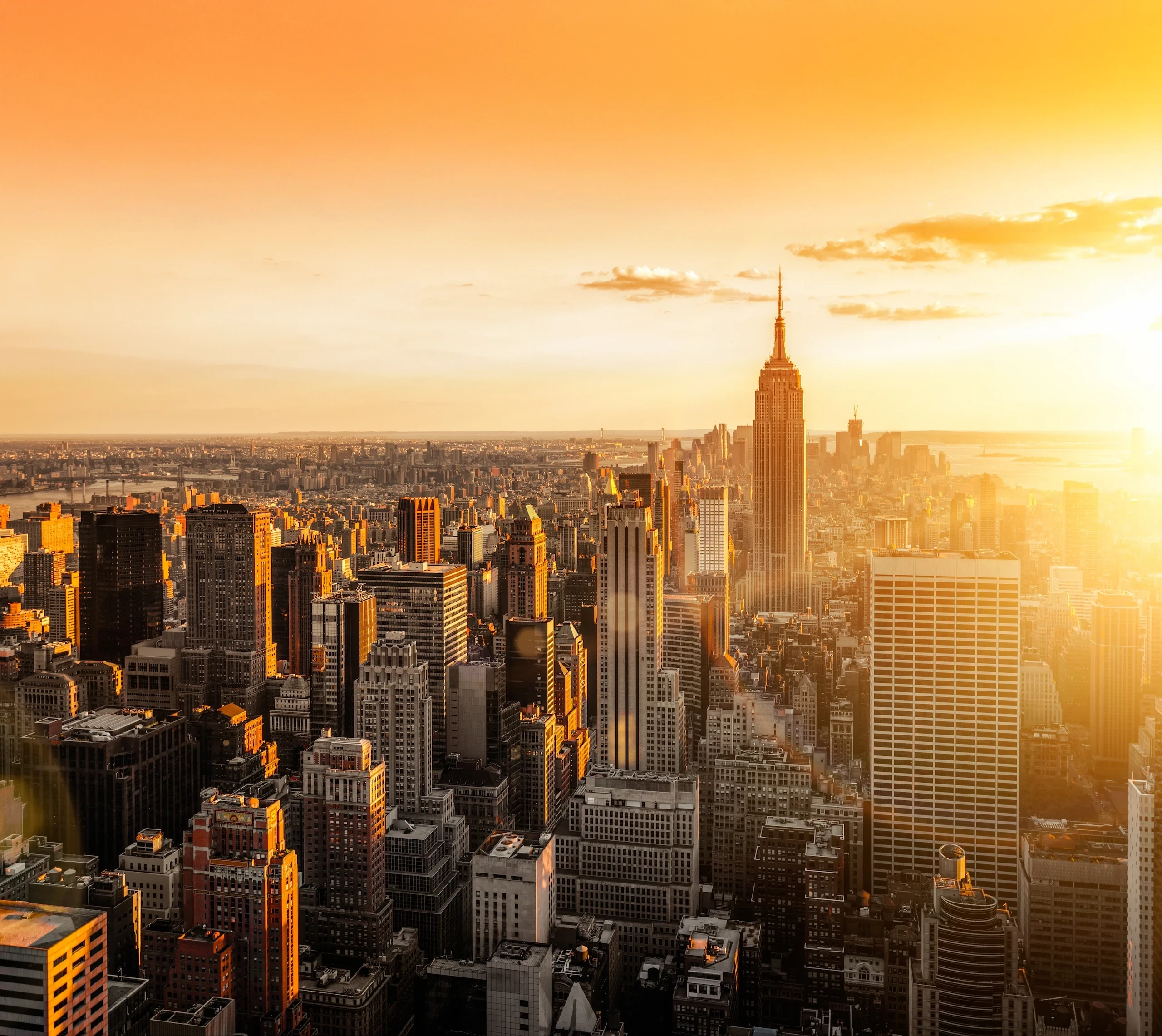 Aerial view of the NYC skyline at sunrise, capturing iconic skyscrapers and the glowing cityscape as the sun rises over Manhattan.
