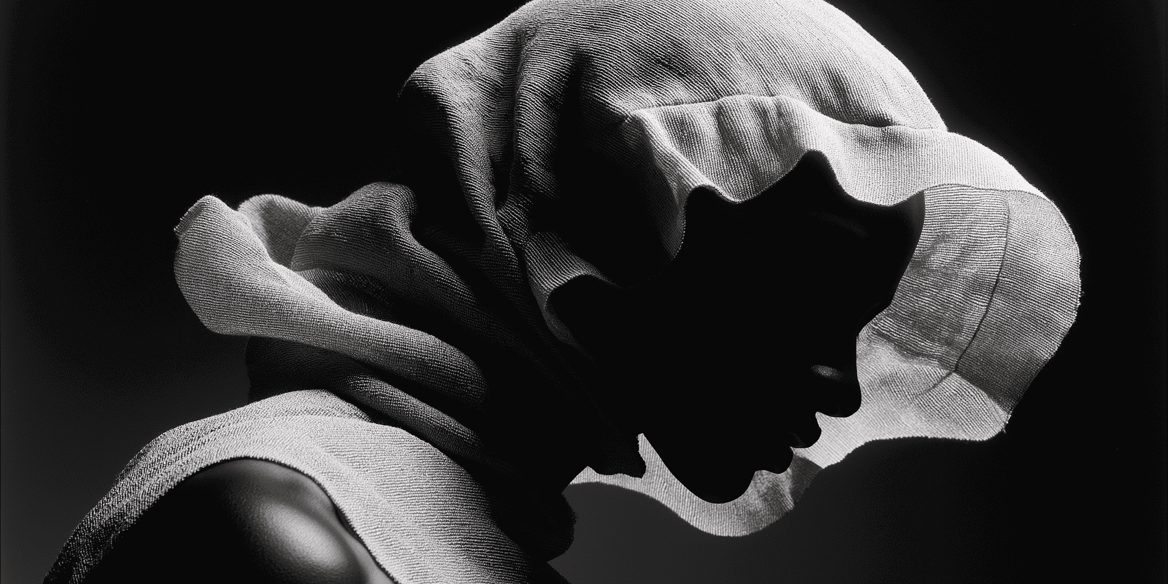 Dramatic side portrait of a hooded figure in grayscale with strong shadows
