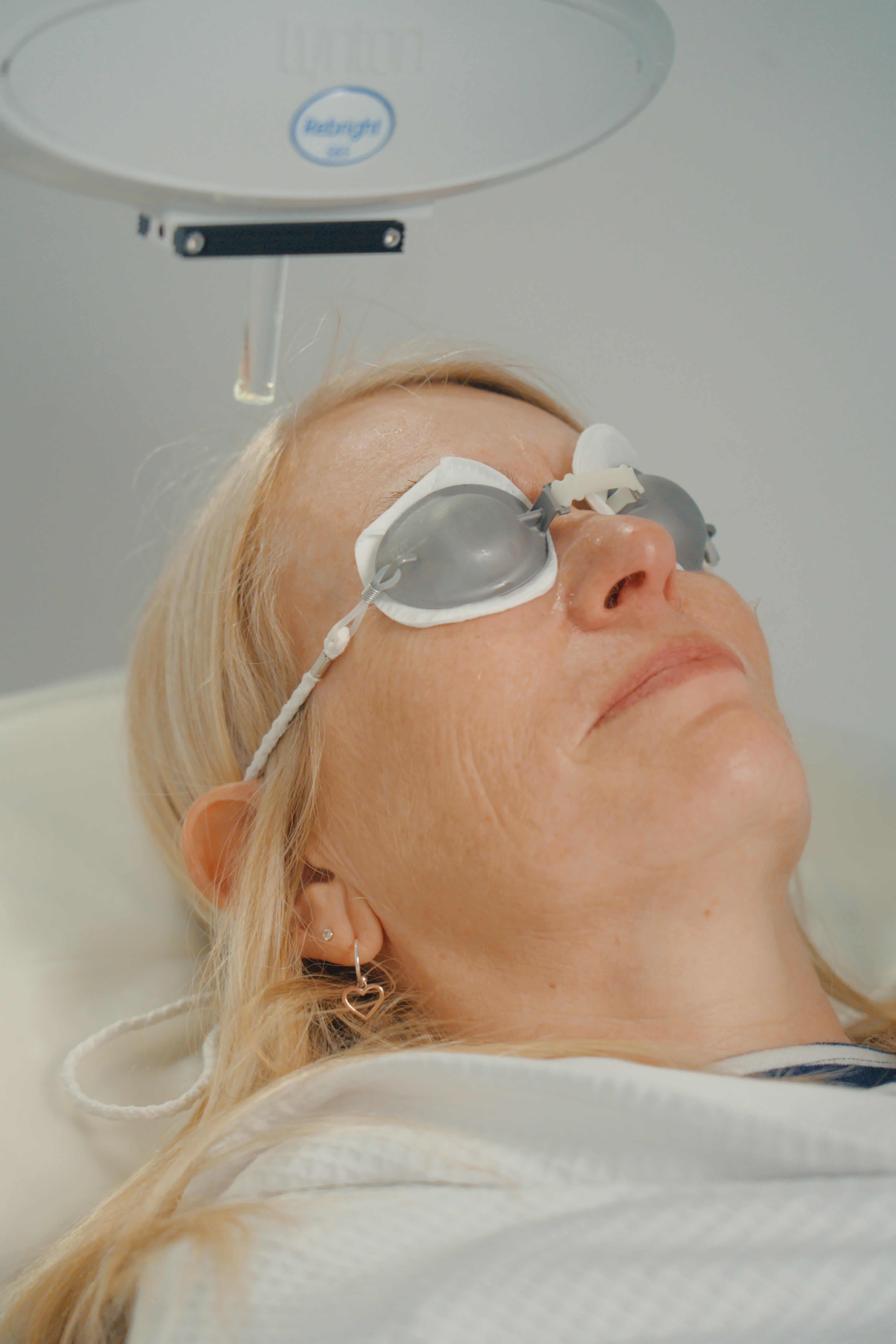 Woman wearing protective eyewear under a light therapy device.