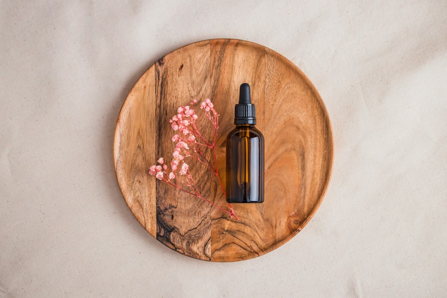 A small bottle of massage oil on a round wooden board with dried pink flowers