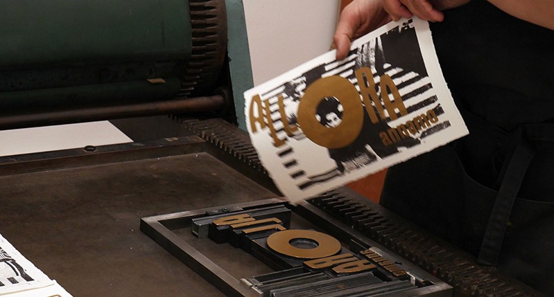 Brown, black and white poster alongside a press that made it.