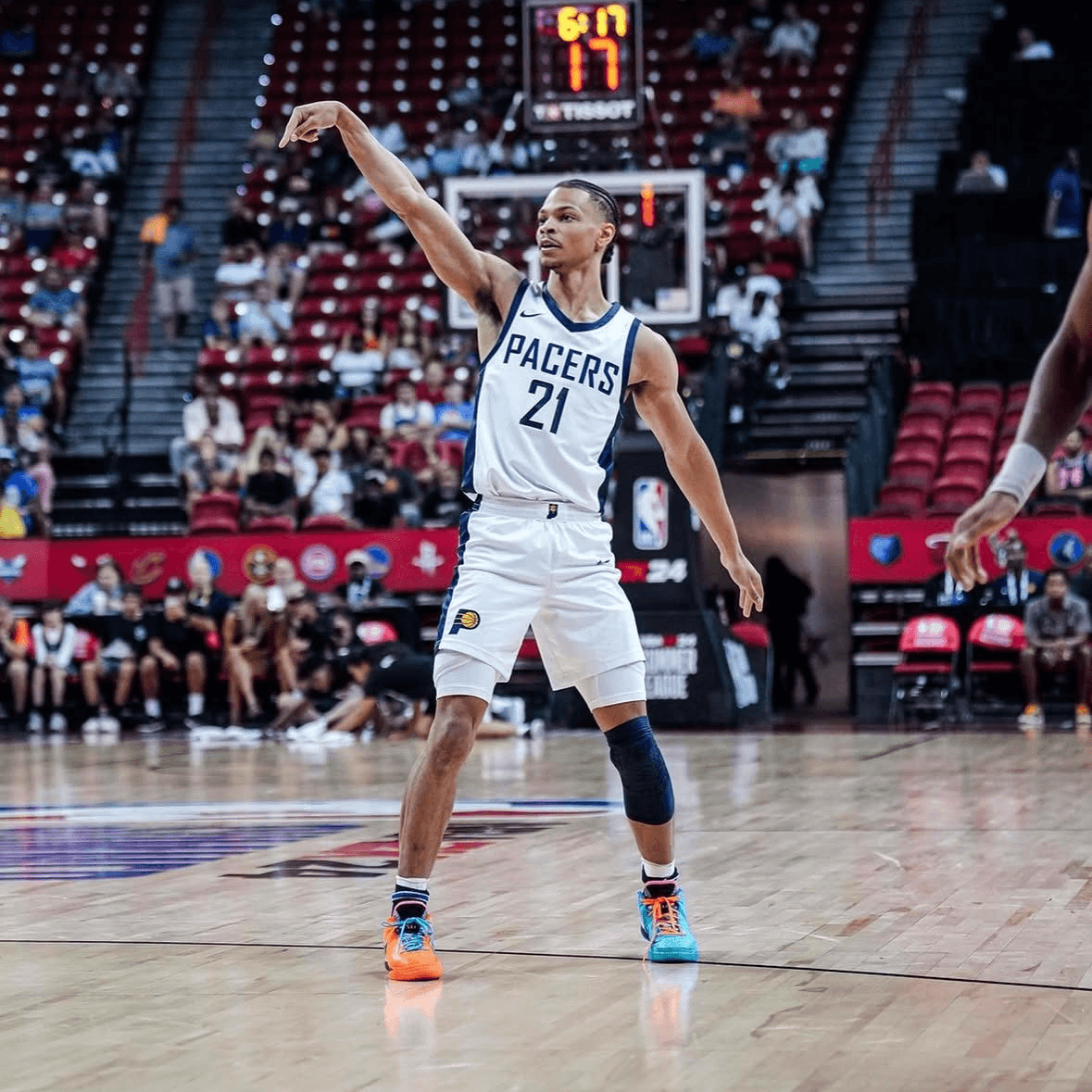 Isaiah Wong in a Pacers uniform, number 21, poses after taking a shot on an indoor court. The stands behind are partially filled with spectators.
