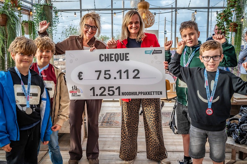 Cordaid-directeur Heleen van den Berg en Hella van der Wijst met kinderen houden cheque vast met daarop het opgehaalde bedrag van de Cordaid Beach Challenge 2026: €75.112 