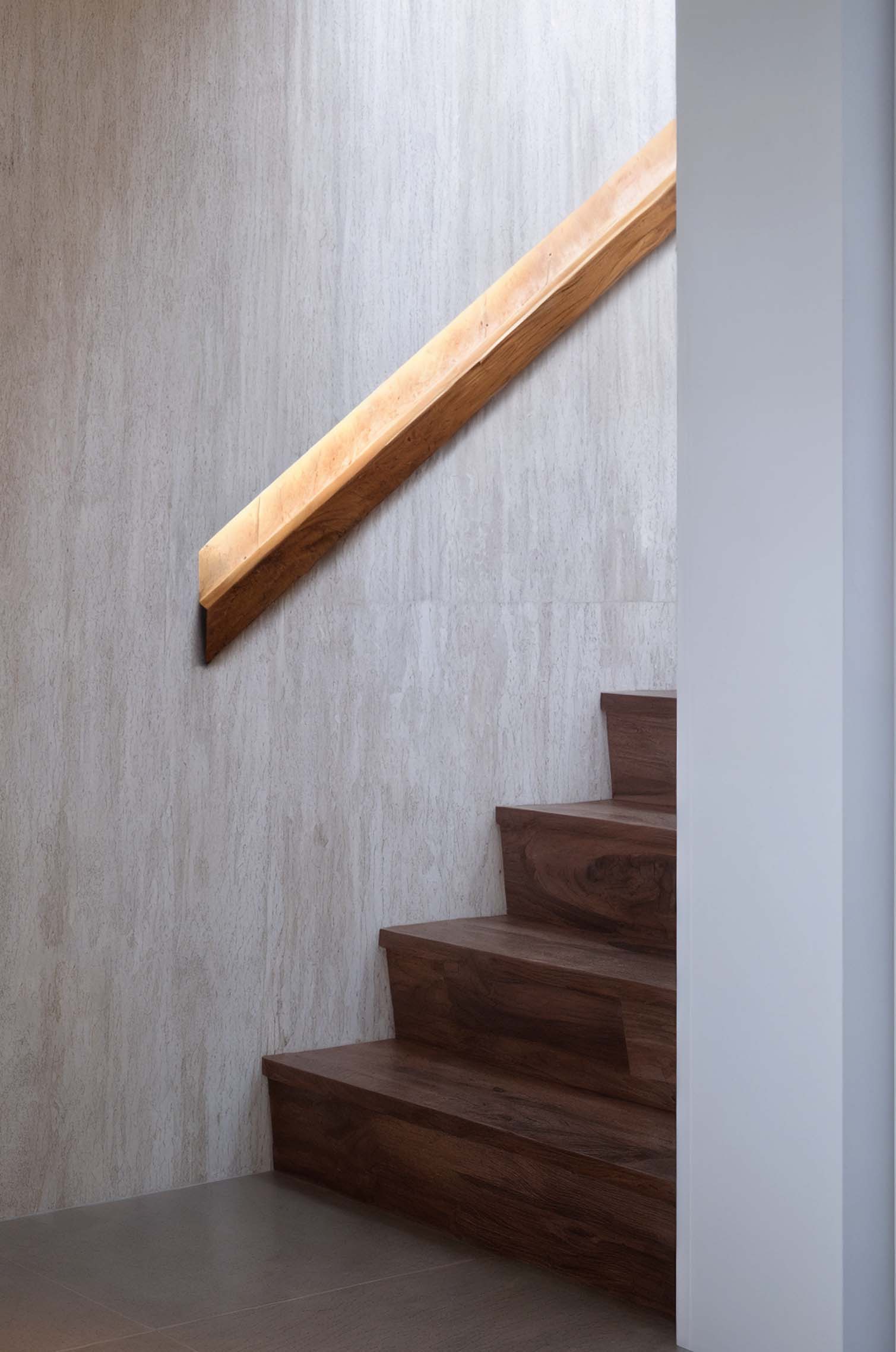 深色實木階梯搭配簡約木質扶手與淺色石材牆面，展現現代建築中的材料對比與簡約美感