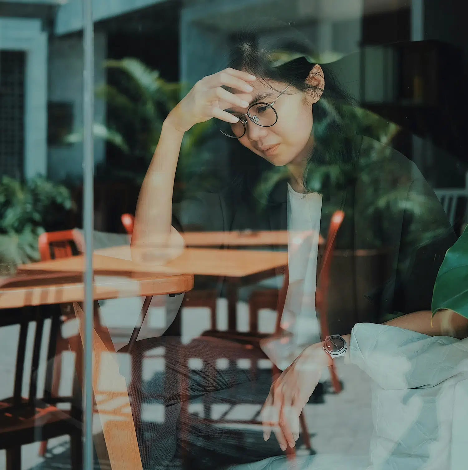 Person sitting alone by a window with hand on forehead, reflecting signs of depression and the need for therapy support in Los Angeles