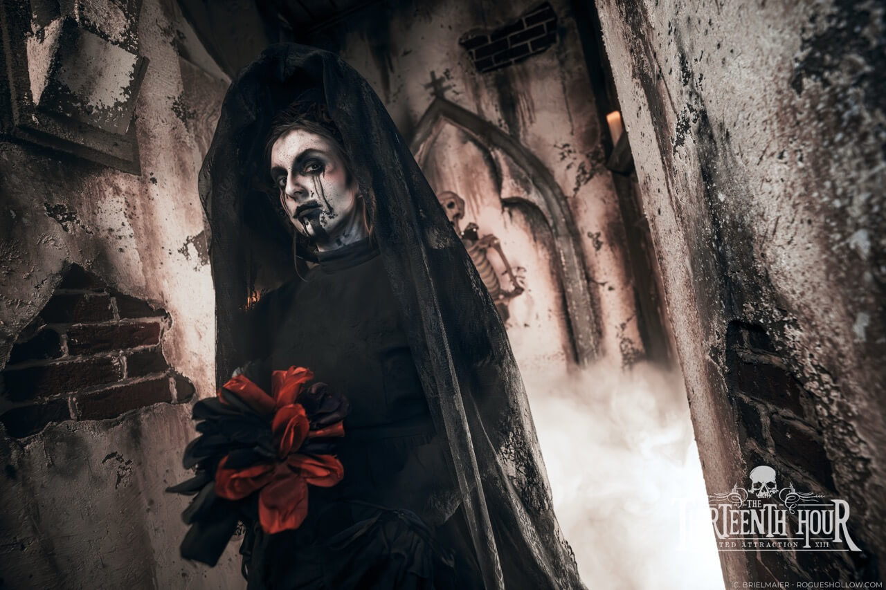 Veiled scare actor holding red flowers in a crumbling corridor