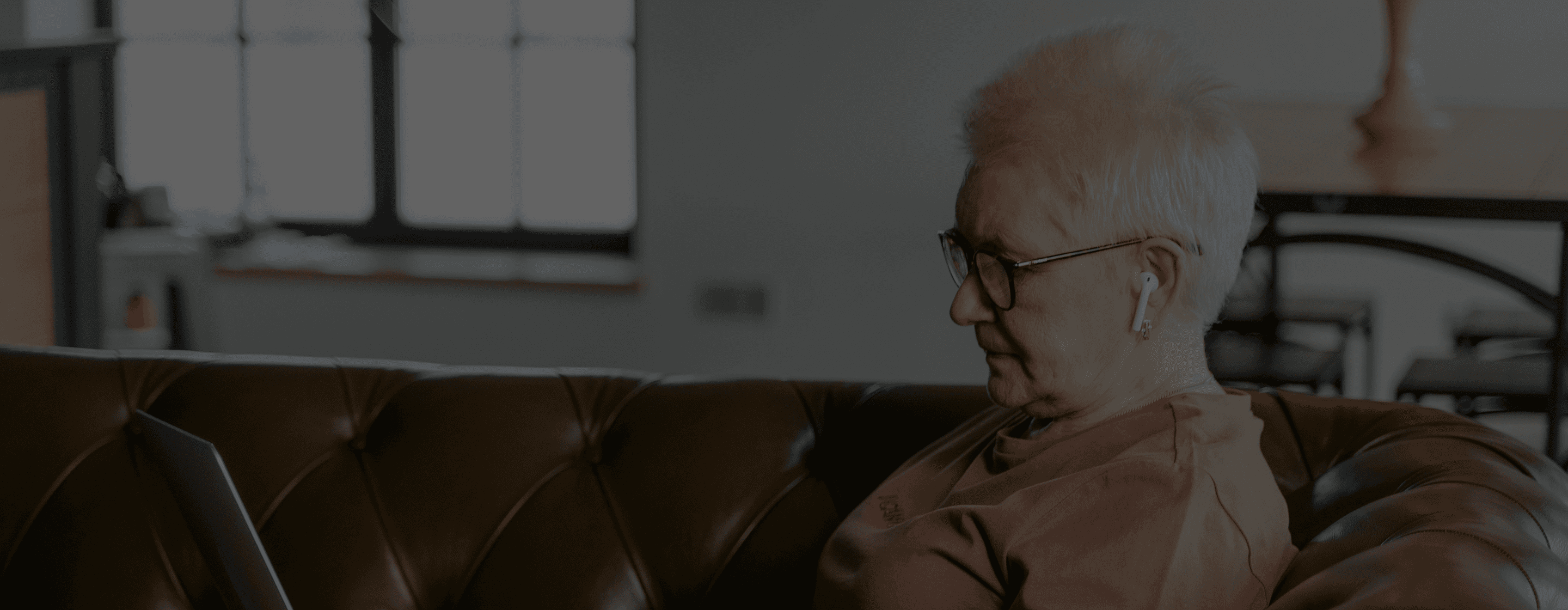 An elderly woman sitting on her couch, using her laptop