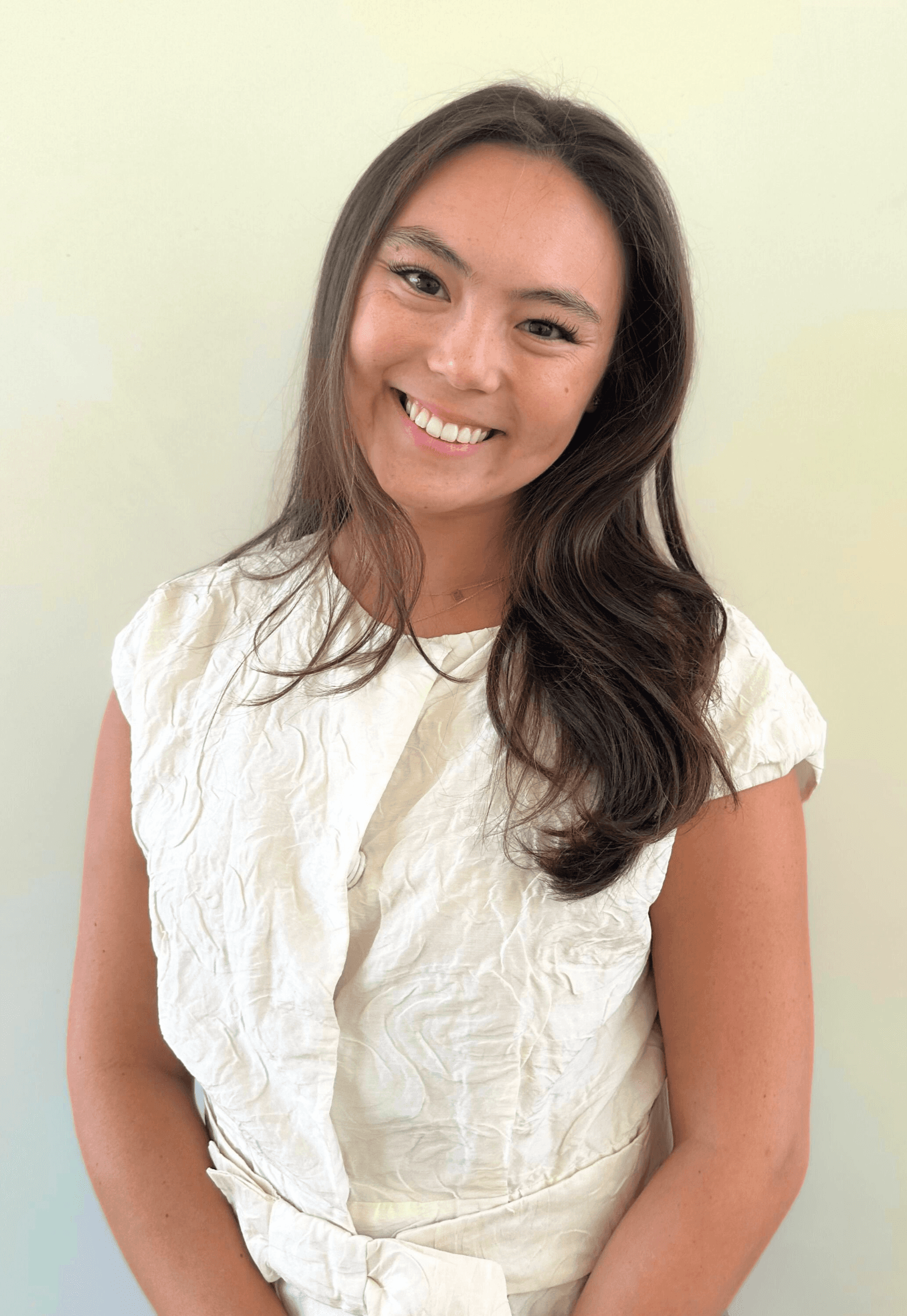 Portrait of Alexis Hedley, Campaign Manager at Playkit, smiling in front of a beige wall and wearing a black strapless top with a gold cross necklace.