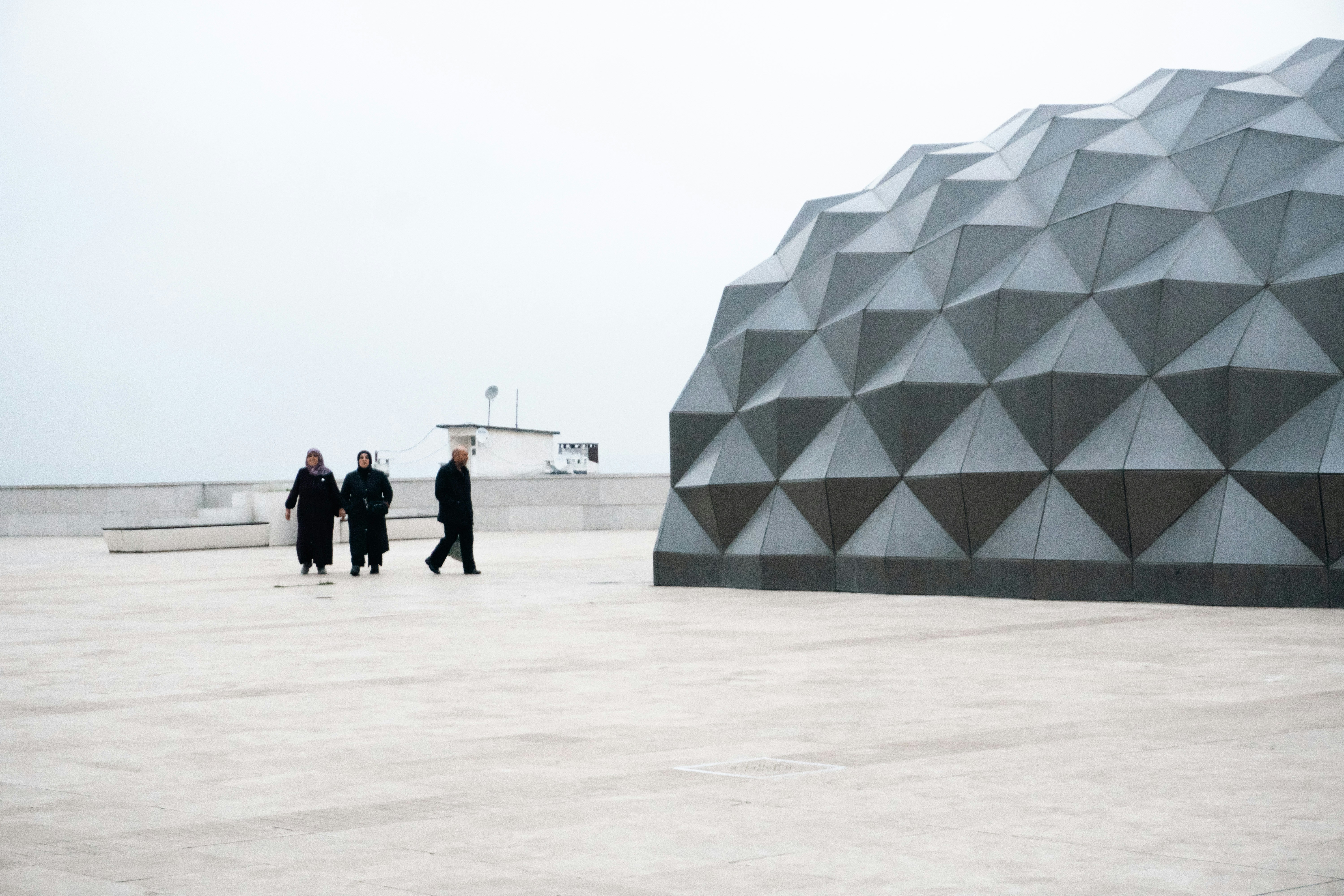 Three people walk near a geometric modern building.