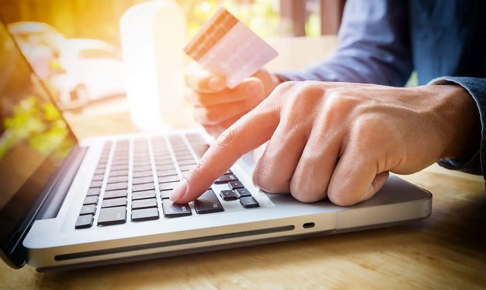 Close-up of a person holding a credit card while typing on a laptop to complete an online purchase.
