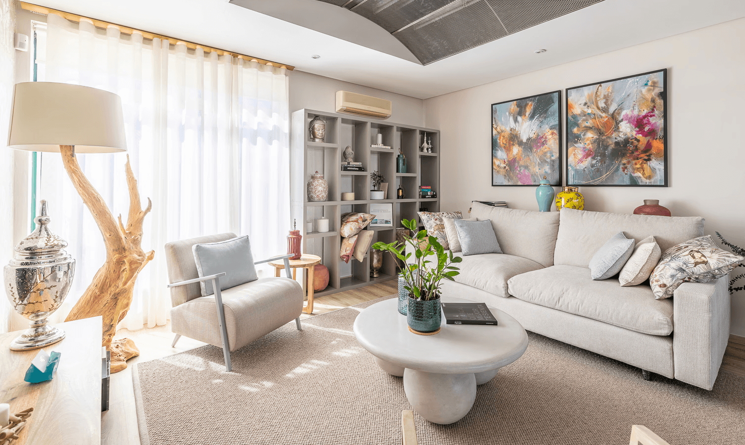 Bright modern showroom featuring a white sofa, artwork, a coffee table, and large windows allowing natural light.