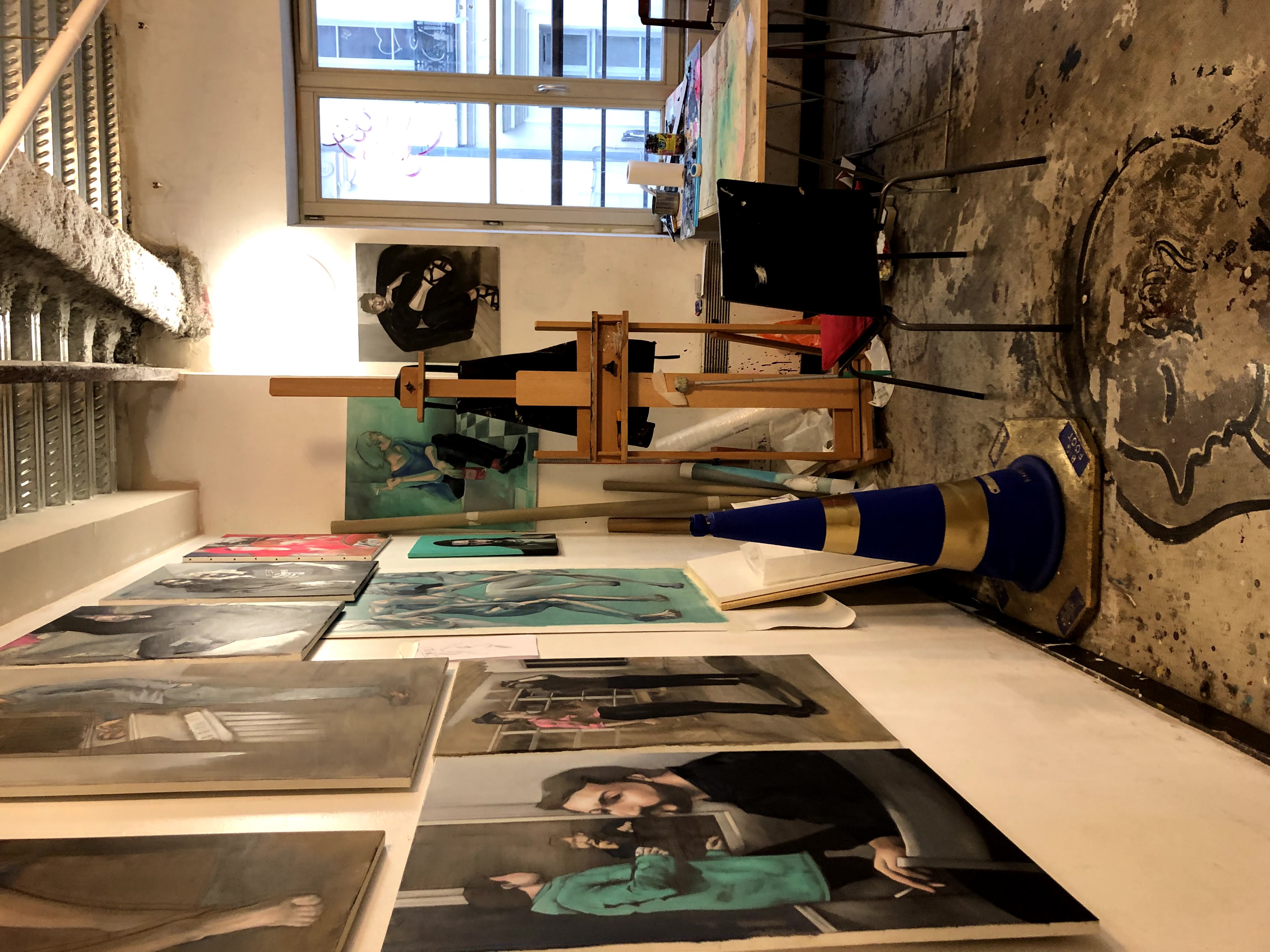 Art studio interior with framed paintings on the wall and an easel in the center.