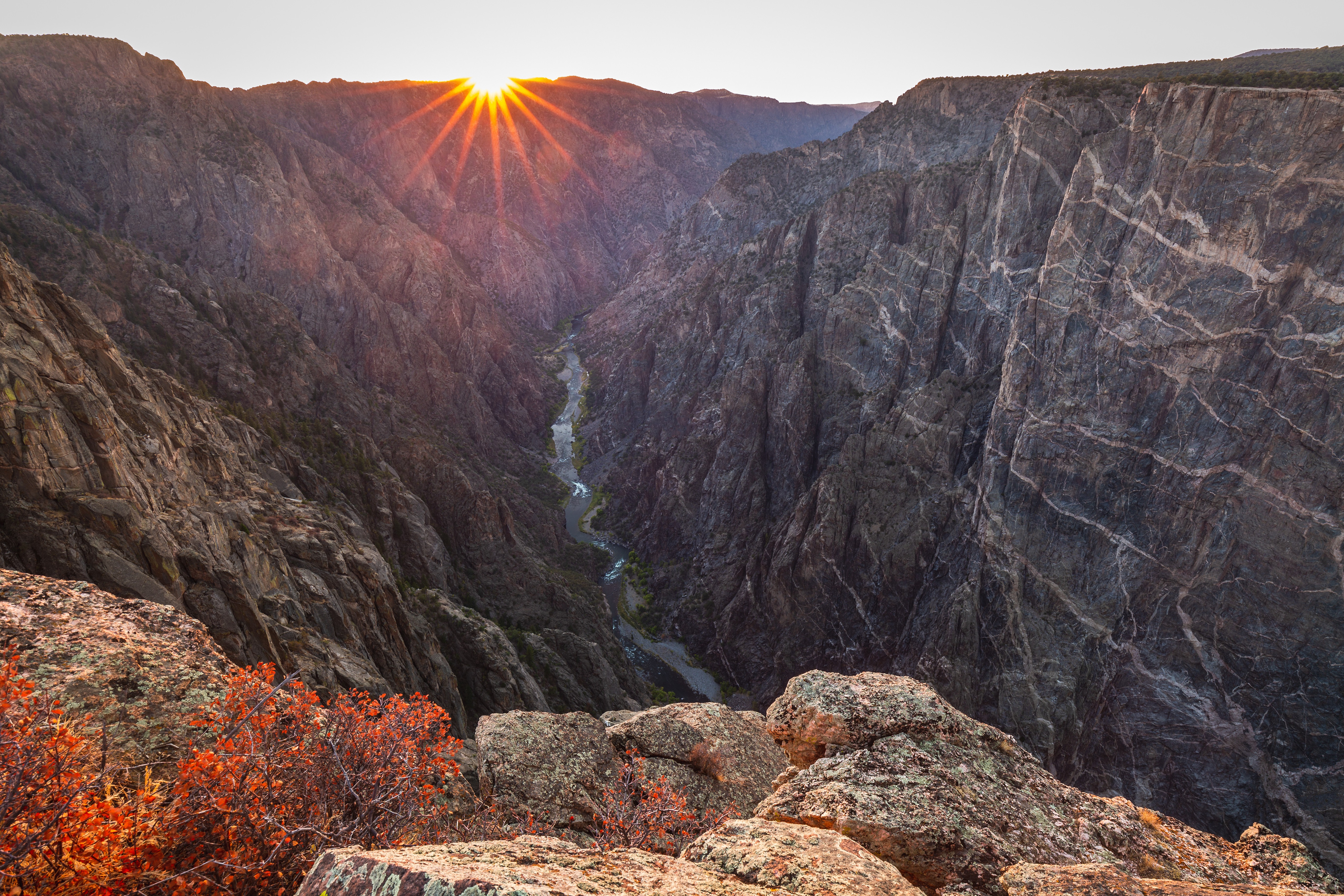 The sun rises over the sheer, veined walls of the Black Canyon of the Gunnison, USA, and the river far below