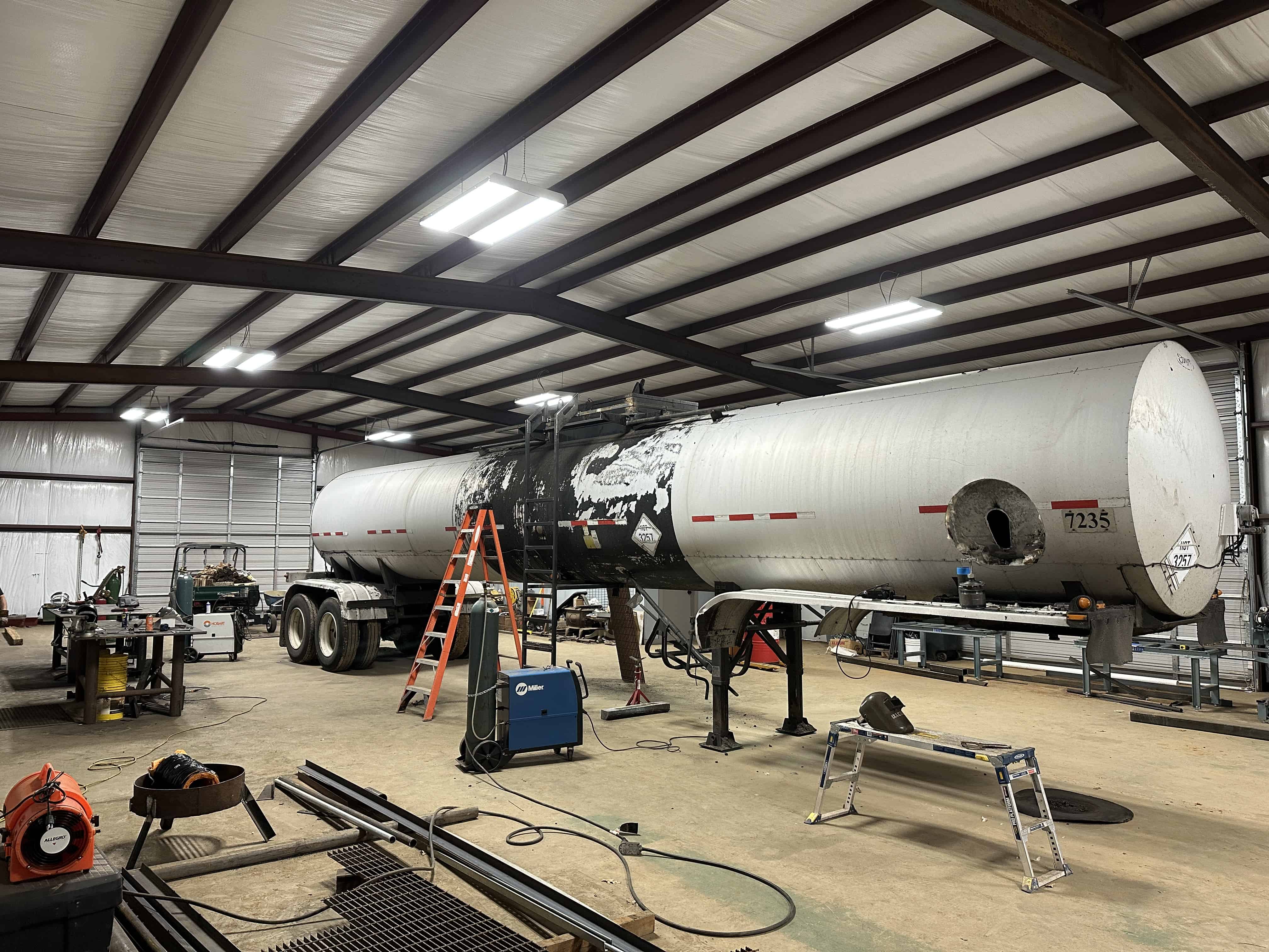 We have an 18 wheeler trailer in our shop.  We are adding a crows nest, ladder, and a bumper to this trailer.  We weld up steel tubing and fit it to the bumper.  Our Miller welding machine and Hobart welding machine are both shown. MIG welding services complete this project in Henderson, Texas.